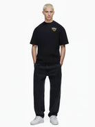 Eine Person mit kurzen blonden Haaren blickt nach vorne und trägt das trueprodigy Hajin Oversize-T-Shirt mit Spray-Smiley & Rückenprint "Happy Mind", gepaart mit schwarzen Jeans und weißen Turnschuhen, vor einem schlichten weißen Hintergrund.