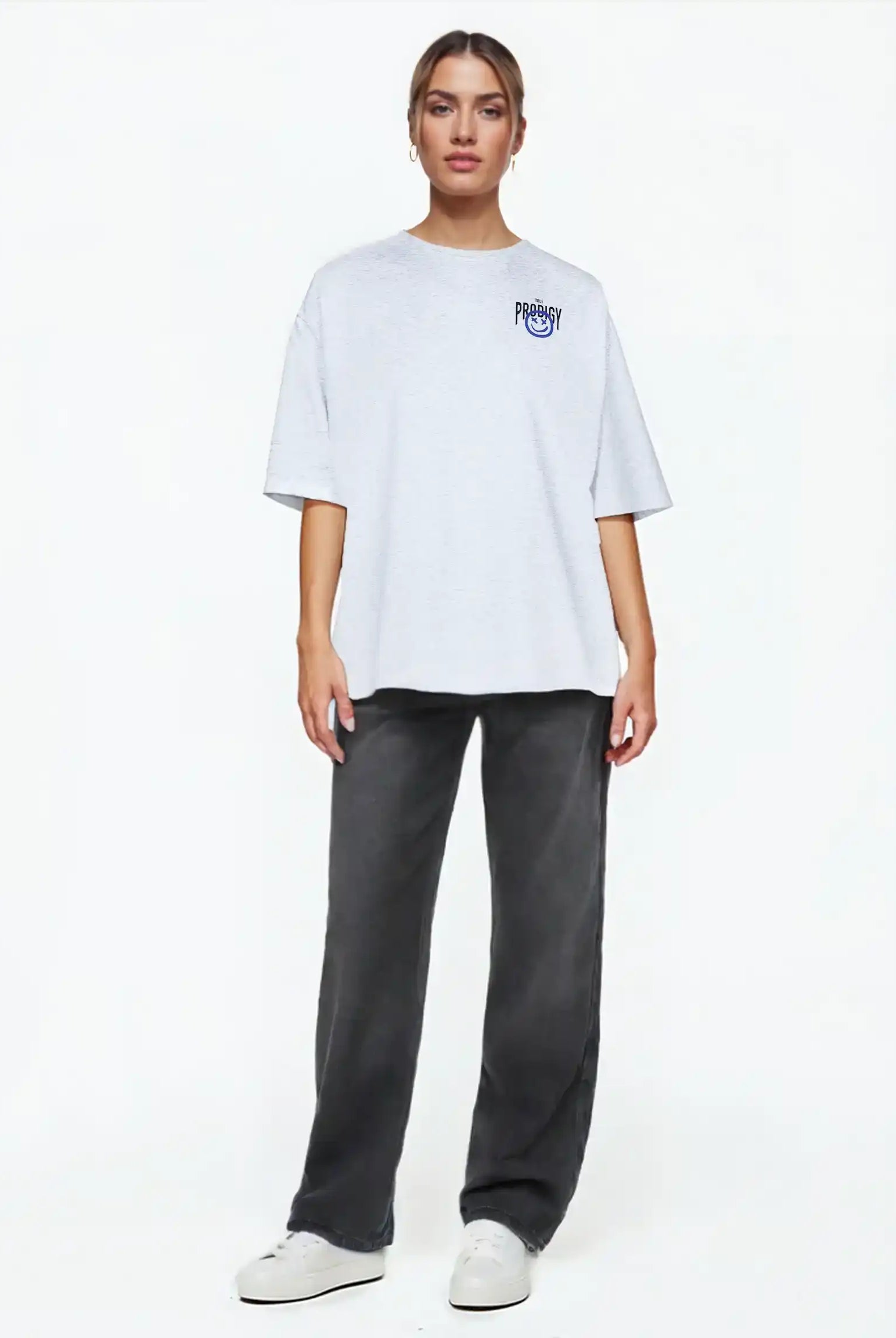 Eine Person steht vor einem weißen Hintergrund, trägt das trueprodigy Hajin F Oversize-T-Shirt mit Spray-Smiley & Happy-Mind-Print, dunkelgraue Jeans und weiße Turnschuhe, blickt nach vorne und hat einen neutralen Blick.