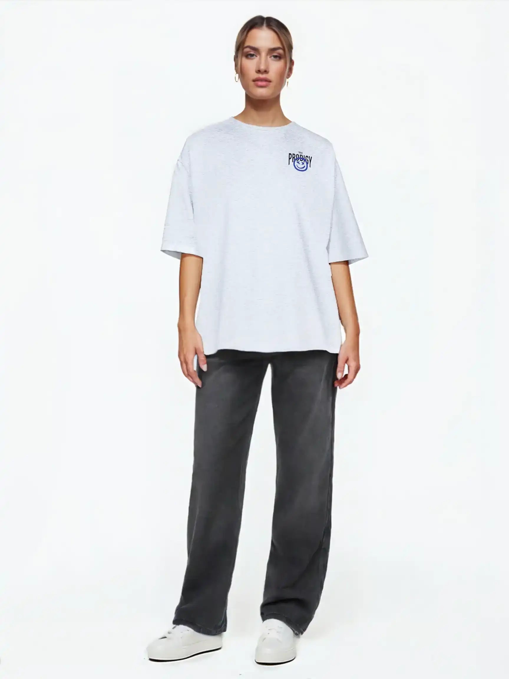 Eine Person steht vor einem weißen Hintergrund, trägt das trueprodigy Hajin F Oversize-T-Shirt mit Spray-Smiley & Happy-Mind-Print, dunkelgraue Jeans und weiße Turnschuhe, blickt nach vorne und hat einen neutralen Blick.