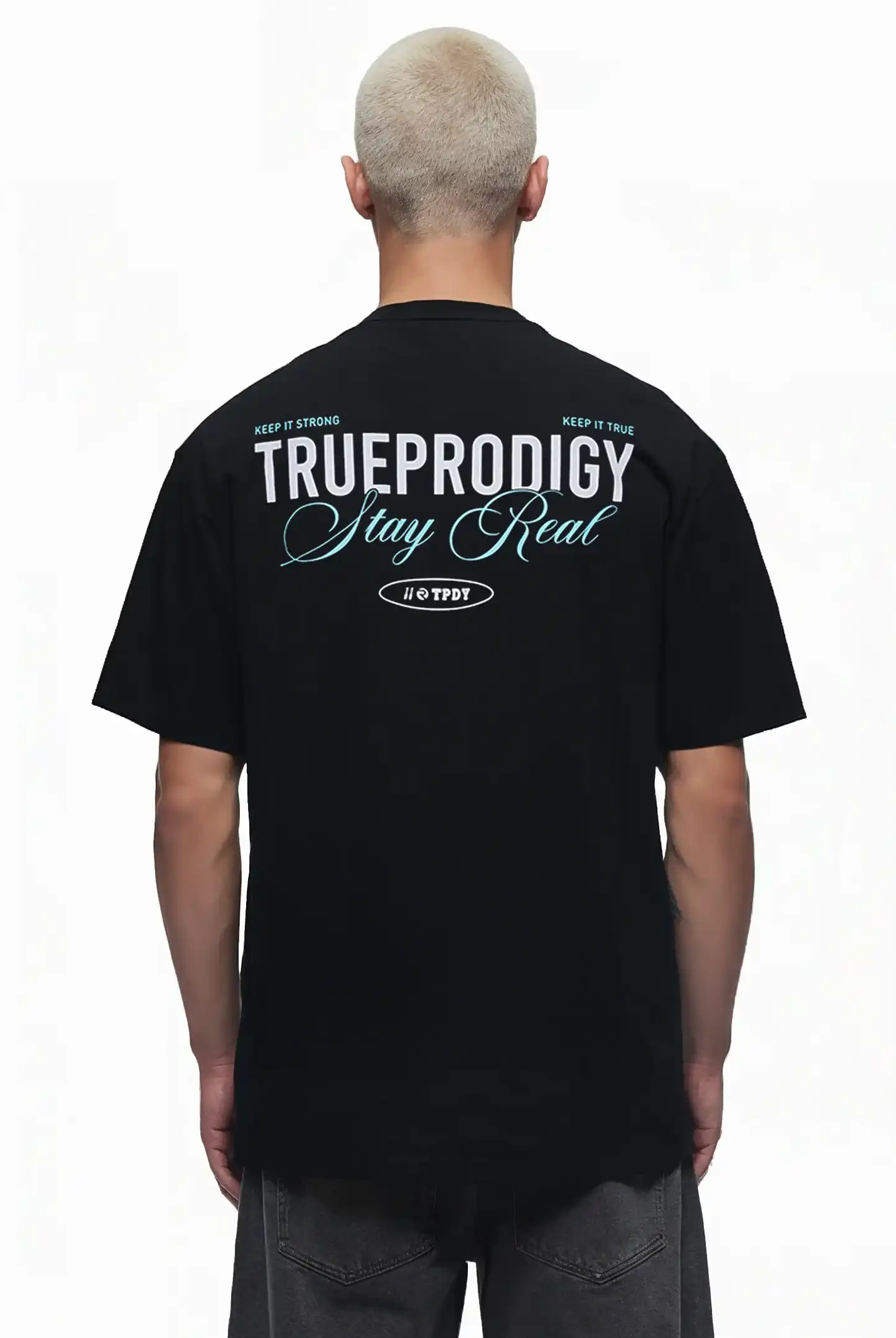 Eine Person mit kurzen blonden Haaren trägt von hinten das trueprodigy Lou Oversize-T-Shirt mit Schriftzug & "Stay Real" Front- & Rückenprint, mit weißem und blauem Druck auf dem oberen Rücken.