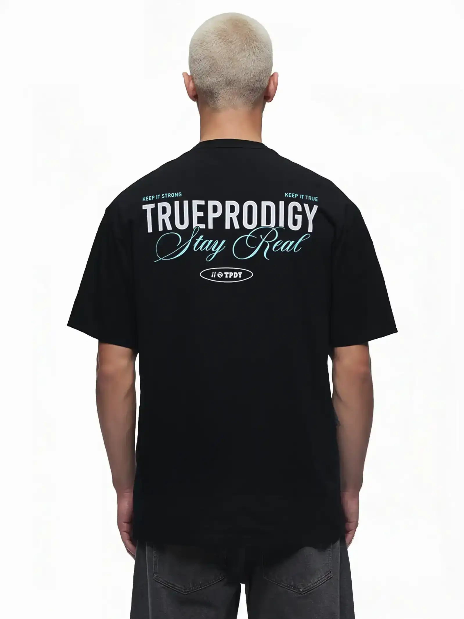 Eine Person mit kurzen blonden Haaren trägt von hinten das trueprodigy Lou Oversize-T-Shirt mit Schriftzug & "Stay Real" Front- & Rückenprint, mit weißem und blauem Druck auf dem oberen Rücken.