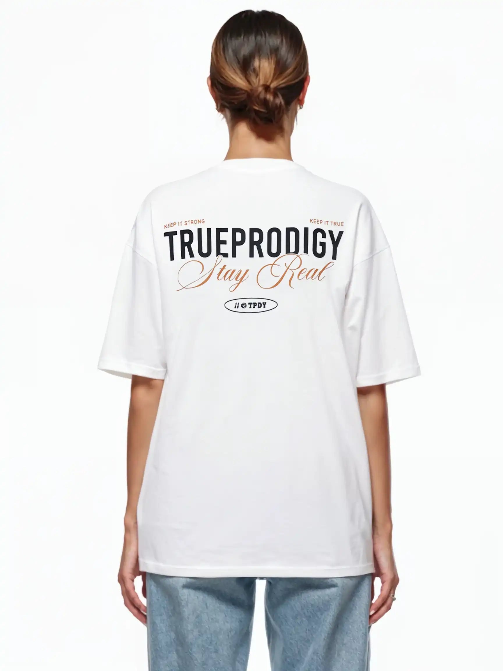 Eine Person blickt von der Kamera weg und trägt ein weißes trueprodigy Lou F Oversize-T-Shirt mit dem Schriftzug "Stay Real" auf Vorder- und Rückseite, gepaart mit einer hellblauen Jeans. Die geräumige Passform hebt sich von dem schlichten weißen Hintergrund ab.