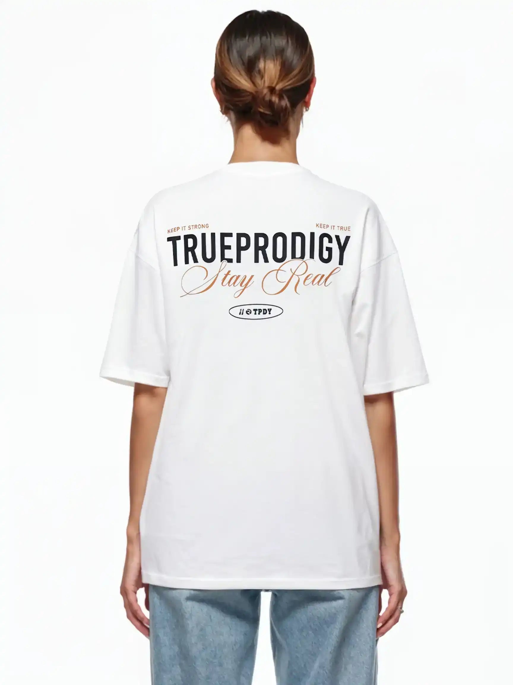 Eine Person blickt von der Kamera weg und trägt ein weißes trueprodigy Lou F Oversize-T-Shirt mit dem Schriftzug "Stay Real" auf Vorder- und Rückseite, gepaart mit einer hellblauen Jeans. Die geräumige Passform hebt sich von dem schlichten weißen Hintergrund ab.