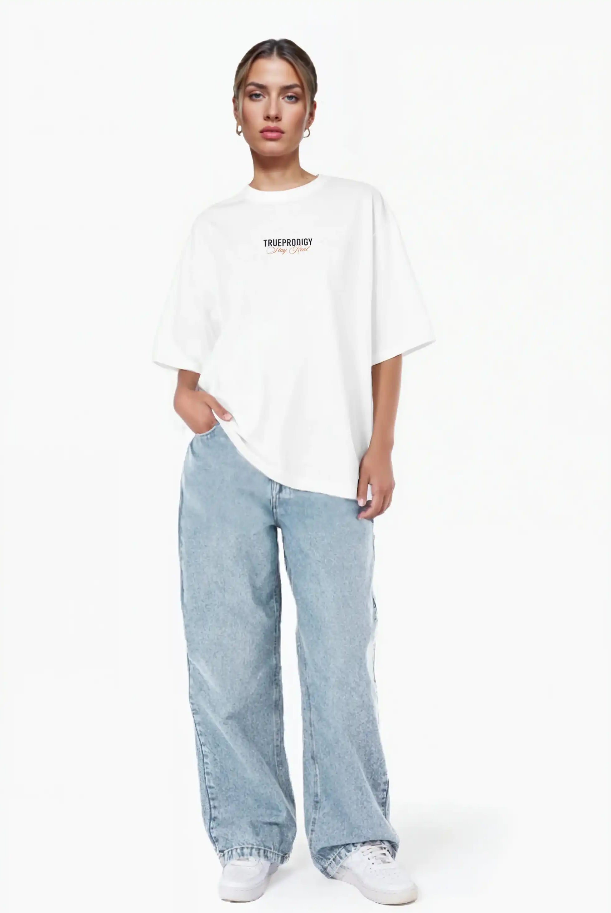 Eine Person steht vor einem weißen Hintergrund und trägt das trueprodigy Lou F Oversize-T-Shirt mit "Stay Real" Schriftzug vorne & hinten und hellblaue Baggy-Jeans, eine Hand in der Tasche, gestylt mit weißen Sneakers.