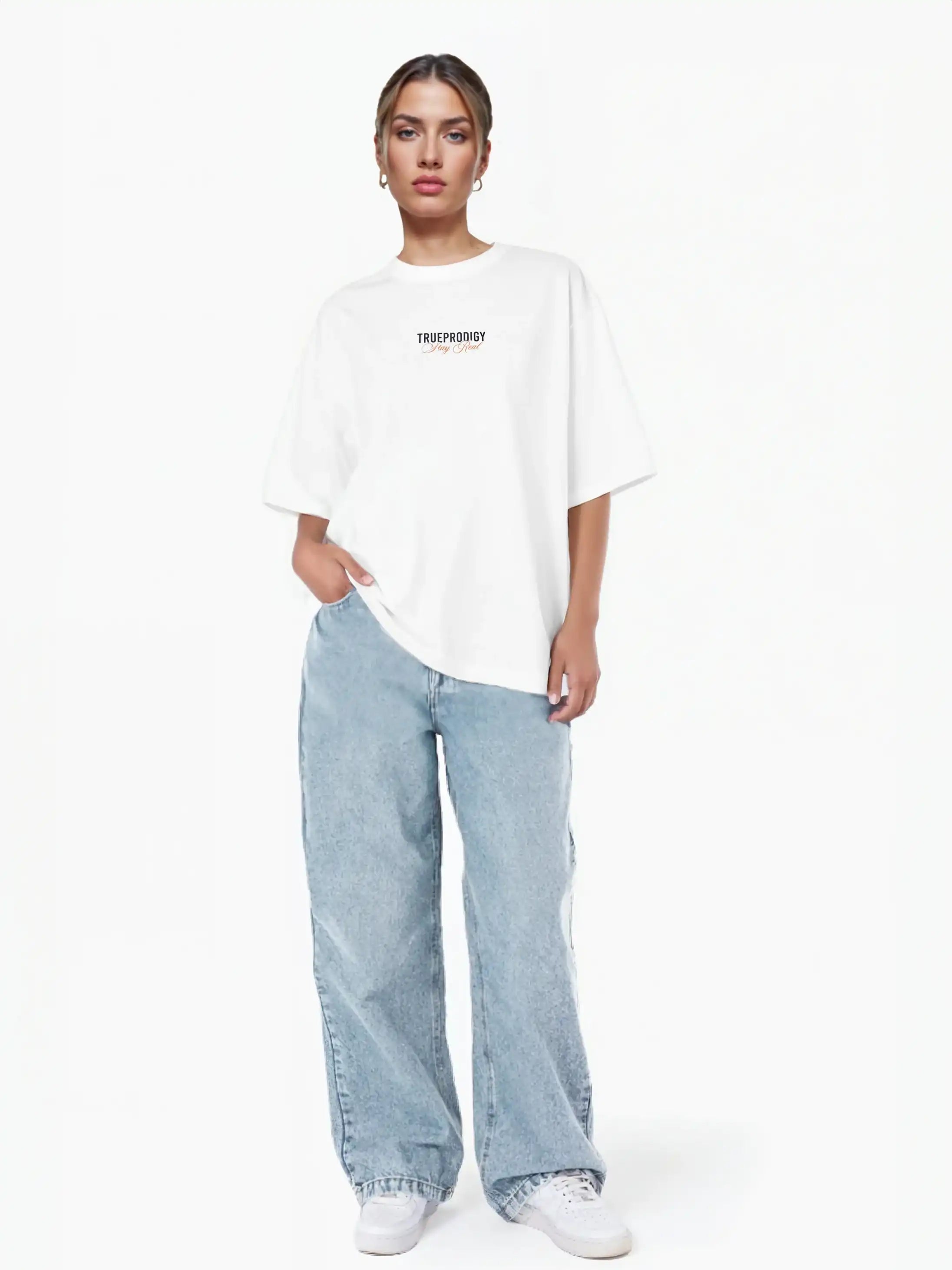 Eine Person steht vor einem weißen Hintergrund und trägt das trueprodigy Lou F Oversize-T-Shirt mit "Stay Real" Schriftzug vorne & hinten und hellblaue Baggy-Jeans, eine Hand in der Tasche, gestylt mit weißen Sneakers.
