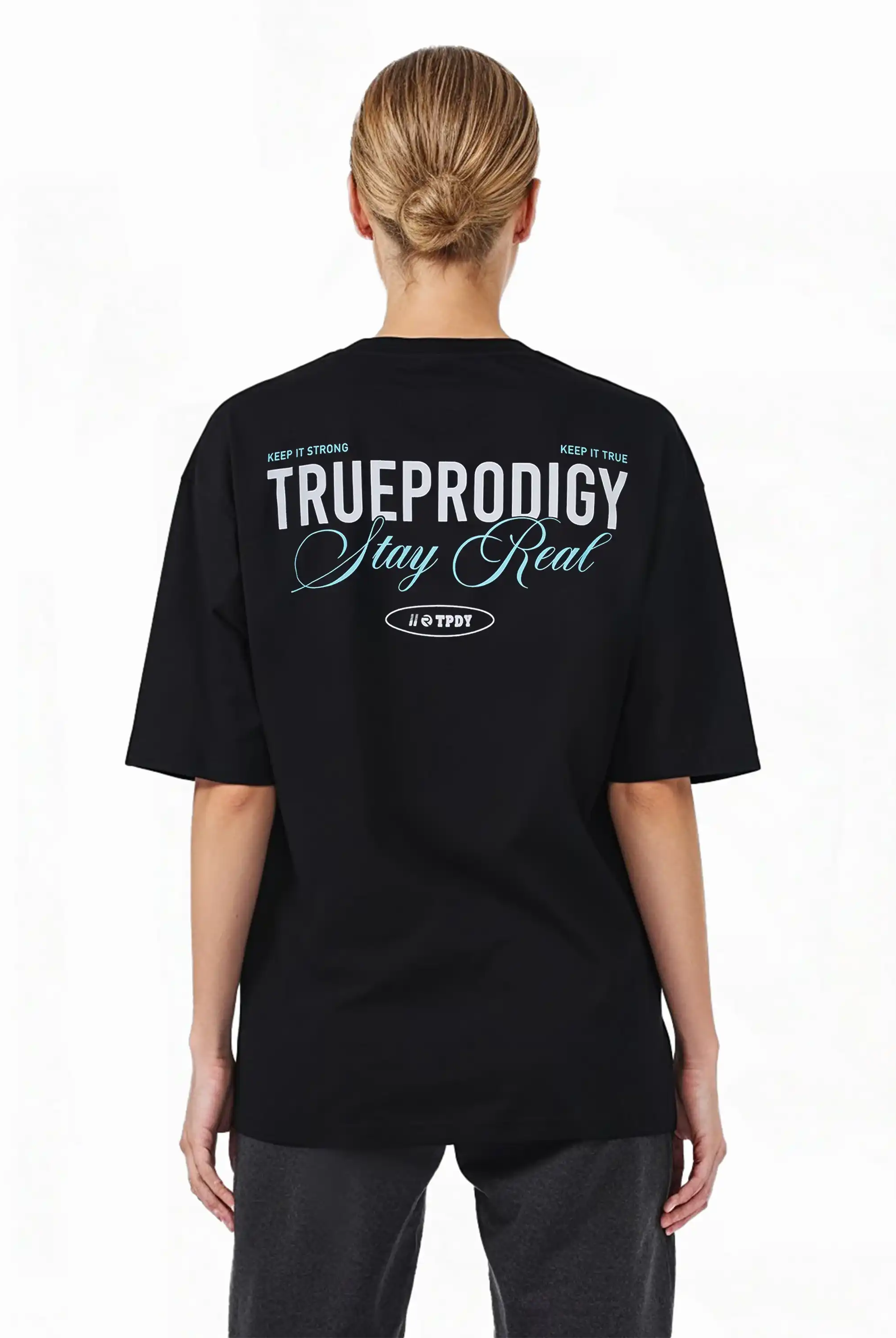 Eine Person mit blonden Haaren in einem tiefen Dutt ist von hinten zu sehen. Sie trägt das trueprodigy Oversize-T-Shirt mit "Stay Real" Schriftzug vorne & hinten, mit weißem und hellblauem Text auf schwerem Jerseystoff.