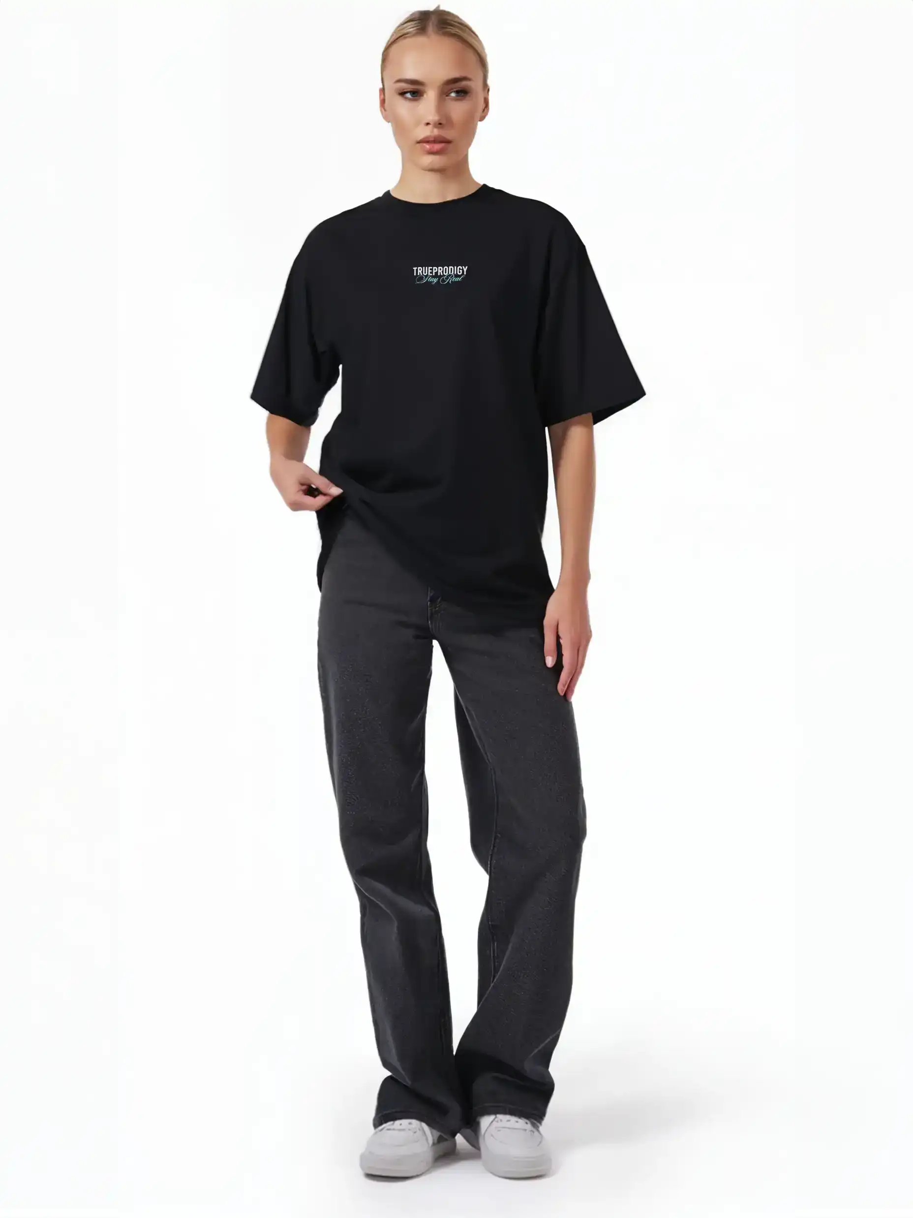 Eine Person steht vor einem schlichten weißen Hintergrund und trägt das trueprodigy Lou F Oversize-T-Shirt mit "Stay Real"-Druck auf Vorder- und Rückseite aus schwerem Jersey, gepaart mit einer dunklen Jeans und weißen Sneakers. Das Unisex-Shirt hat eine kleine Brustgrafik.