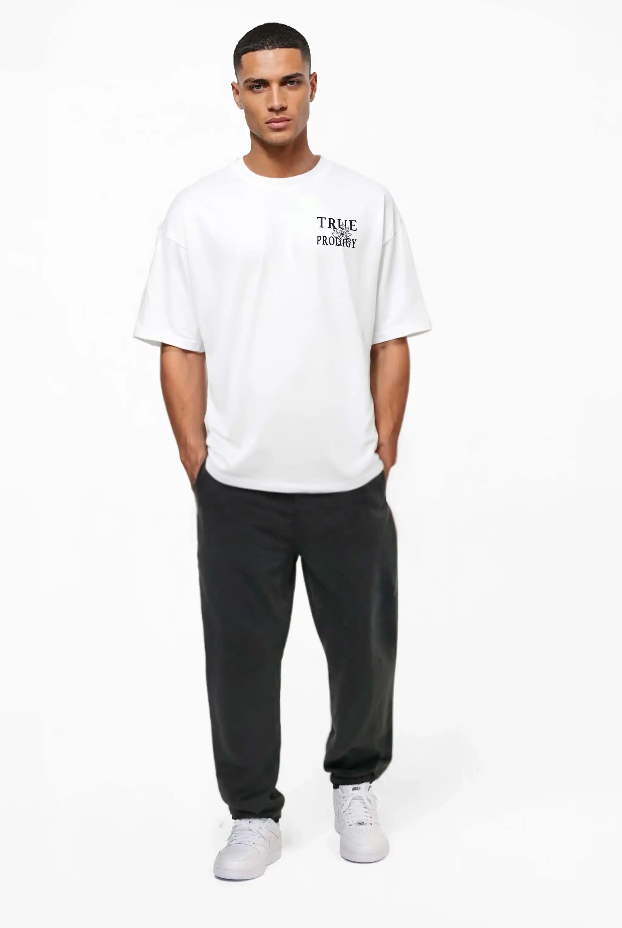 Ein Mann blickt nach vorne und trägt das trueprodigy Alex Oversize-T-Shirt mit Rosen-Skizze & Logo als Front- und Rückenprint, eine dunkle Hose und weiße Sneakers. Das Shirt ist aus schwerem Jerseystoff gefertigt. Er steht vor einem schlichten weißen Hintergrund und hat die Hände in den Taschen.