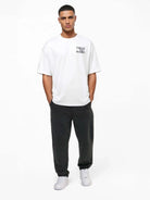 Ein Mann blickt nach vorne und trägt das trueprodigy Alex Oversize-T-Shirt mit Rosen-Skizze & Logo als Front- und Rückenprint, eine dunkle Hose und weiße Sneakers. Das Shirt ist aus schwerem Jerseystoff gefertigt. Er steht vor einem schlichten weißen Hintergrund und hat die Hände in den Taschen.