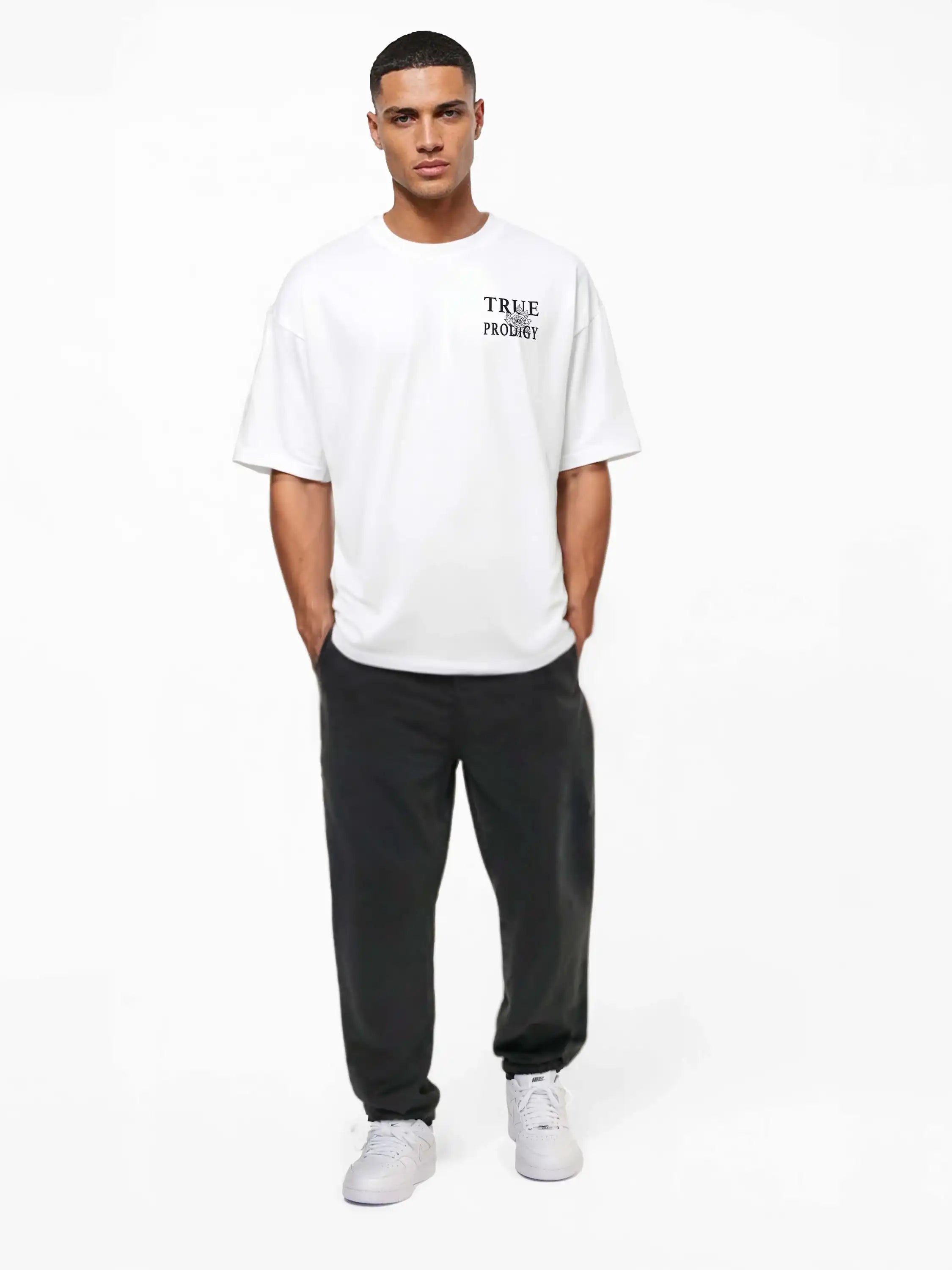 Ein Mann blickt nach vorne und trägt das trueprodigy Alex Oversize-T-Shirt mit Rosen-Skizze & Logo als Front- und Rückenprint, eine dunkle Hose und weiße Sneakers. Das Shirt ist aus schwerem Jerseystoff gefertigt. Er steht vor einem schlichten weißen Hintergrund und hat die Hände in den Taschen.