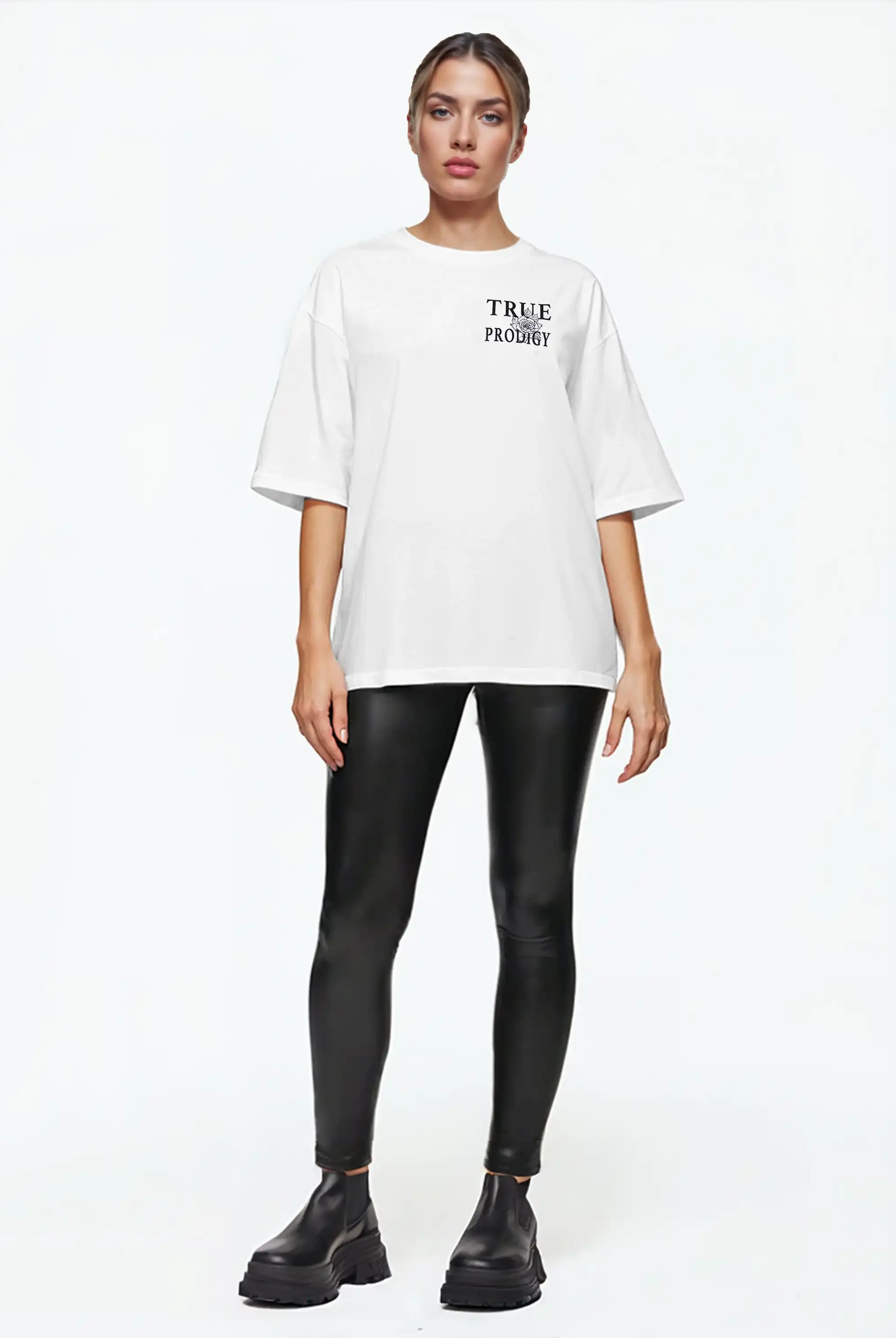 Eine Person steht mit Blick nach vorne in einem weißen trueprodigy Alex F Oversize-T-Shirt mit Spray-Smiley & trueprodigy-Schriftzug auf Vorder- und Rückseite, schwarzen Kunstleder-Leggings und klobigen schwarzen Stiefeln vor einem schlichten weißen Hintergrund.