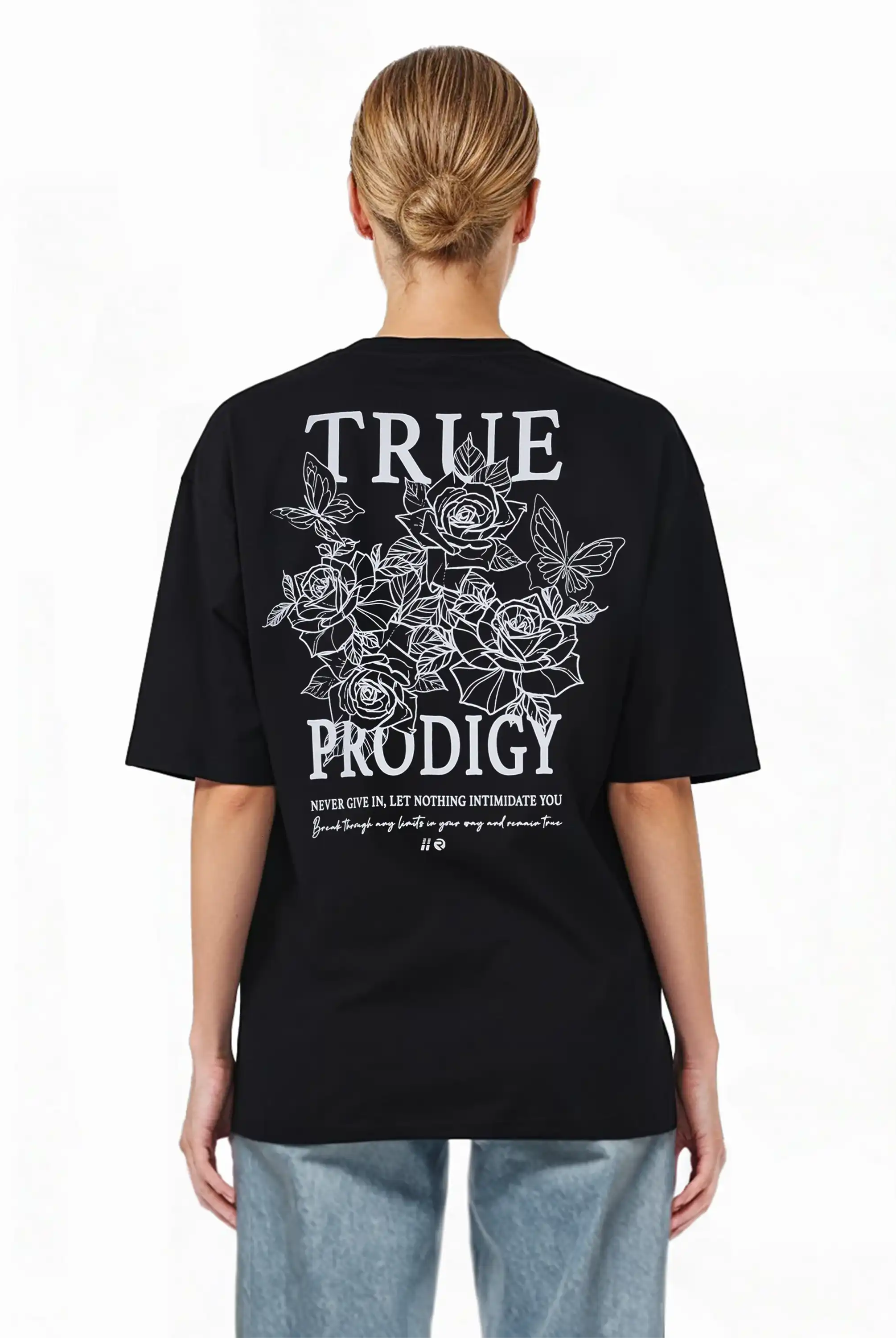 Eine Person mit hellen Haaren in einem tiefen Dutt trägt das schwarze trueprodigy Alex F Oversize-T-Shirt mit einem Spray-Smiley und trueprodigy-Schriftzug auf Vorder- und Rückseite, gepaart mit hellblauen Jeans. Der Hintergrund ist weiß.