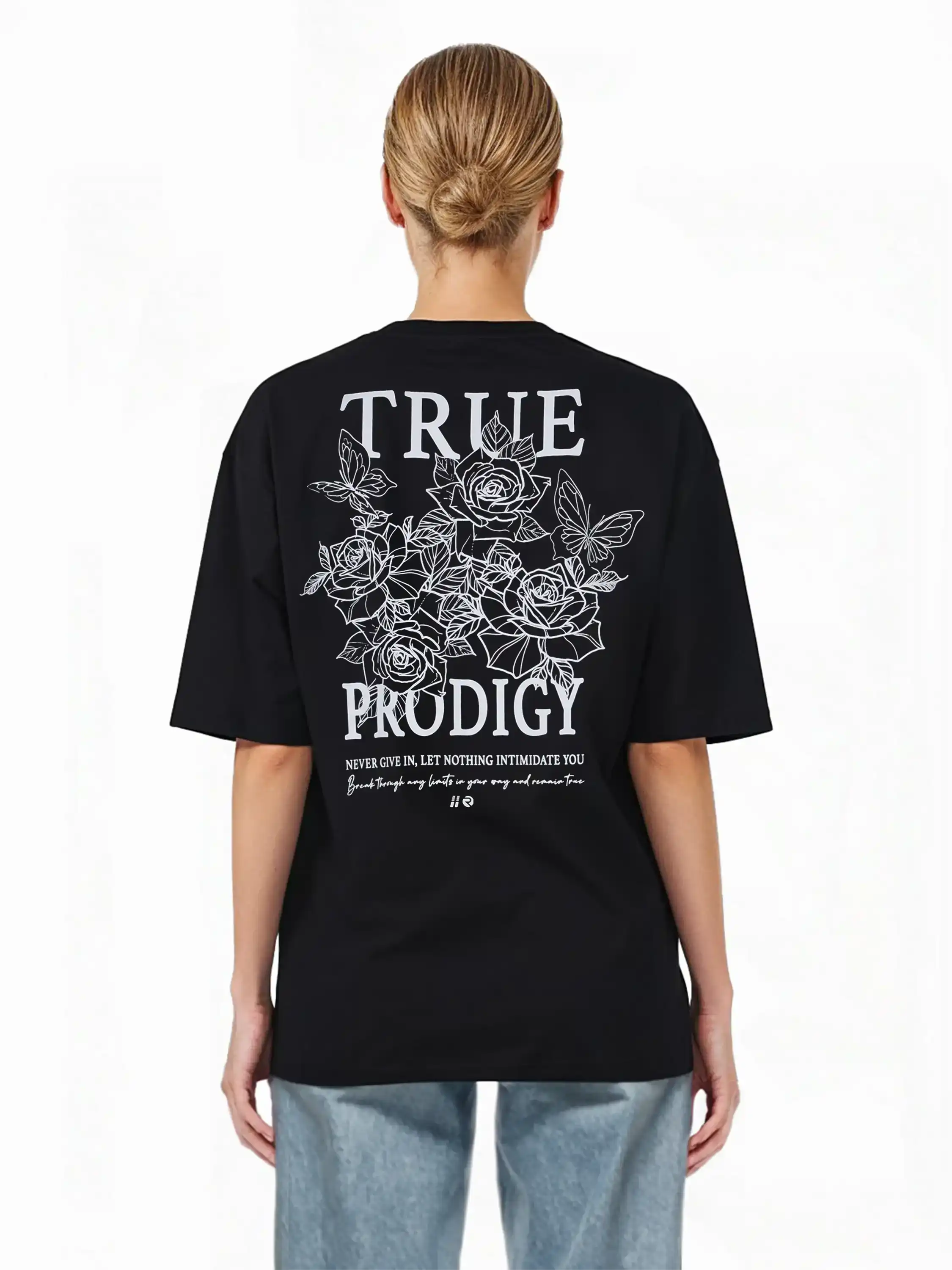 Eine Person mit hellen Haaren in einem tiefen Dutt trägt das schwarze trueprodigy Alex F Oversize-T-Shirt mit einem Spray-Smiley und trueprodigy-Schriftzug auf Vorder- und Rückseite, gepaart mit hellblauen Jeans. Der Hintergrund ist weiß.