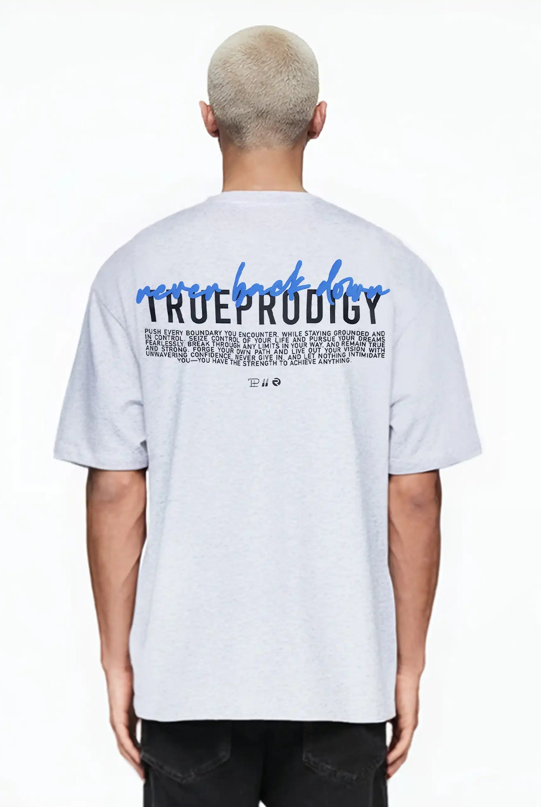 Eine Person mit kurzen, gebleichten blonden Haaren trägt das trueprodigy "Lior" Unisex-T-Shirt in Übergröße in Hellgrau mit einem Logo auf der Brust und einem auffälligen Rückenaufdruck mit "never back down" über dem Namen der Marke.