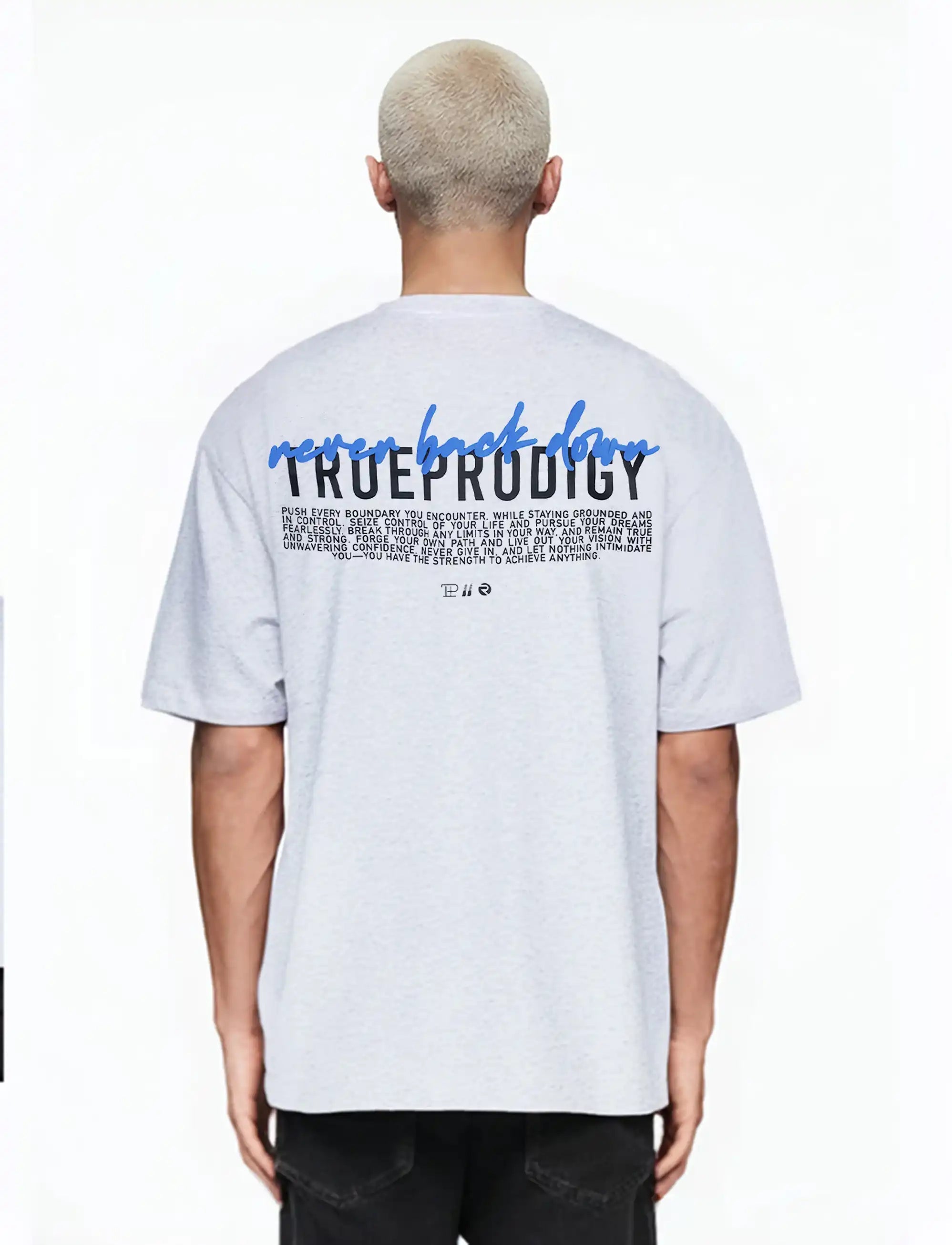 Eine Person mit kurzen, gebleichten blonden Haaren trägt das trueprodigy "Lior" Unisex-T-Shirt in Übergröße in Hellgrau mit einem Logo auf der Brust und einem auffälligen Rückenaufdruck mit "never back down" über dem Namen der Marke.