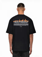 Ein Mann, von hinten gesehen, trägt das Lior Oversize-T-Shirt von trueprodigy, ein schwarzes Unisex-Design mit orangefarbenem und weißem "never back down"-Schriftzug und TRUE PRODIGY-Logo auf dem oberen Rücken, darunter ein kleinerer weißer Schriftzug.