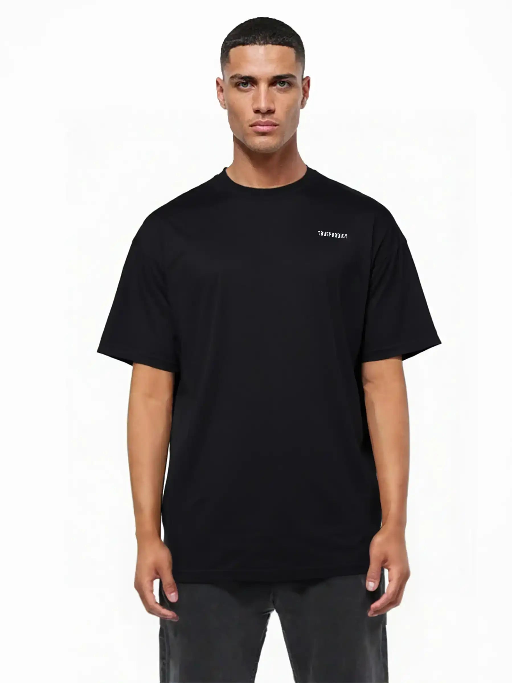 Ein Mann blickt nach vorne, er trägt ein originalgetreues Lior Oversize-T-Shirt aus dickem Jersey in Schwarz mit kleinem weißen Brustlogo und Rückenprint "never back down", dazu dunkle Hose. Der Hintergrund ist weiß und schlicht.