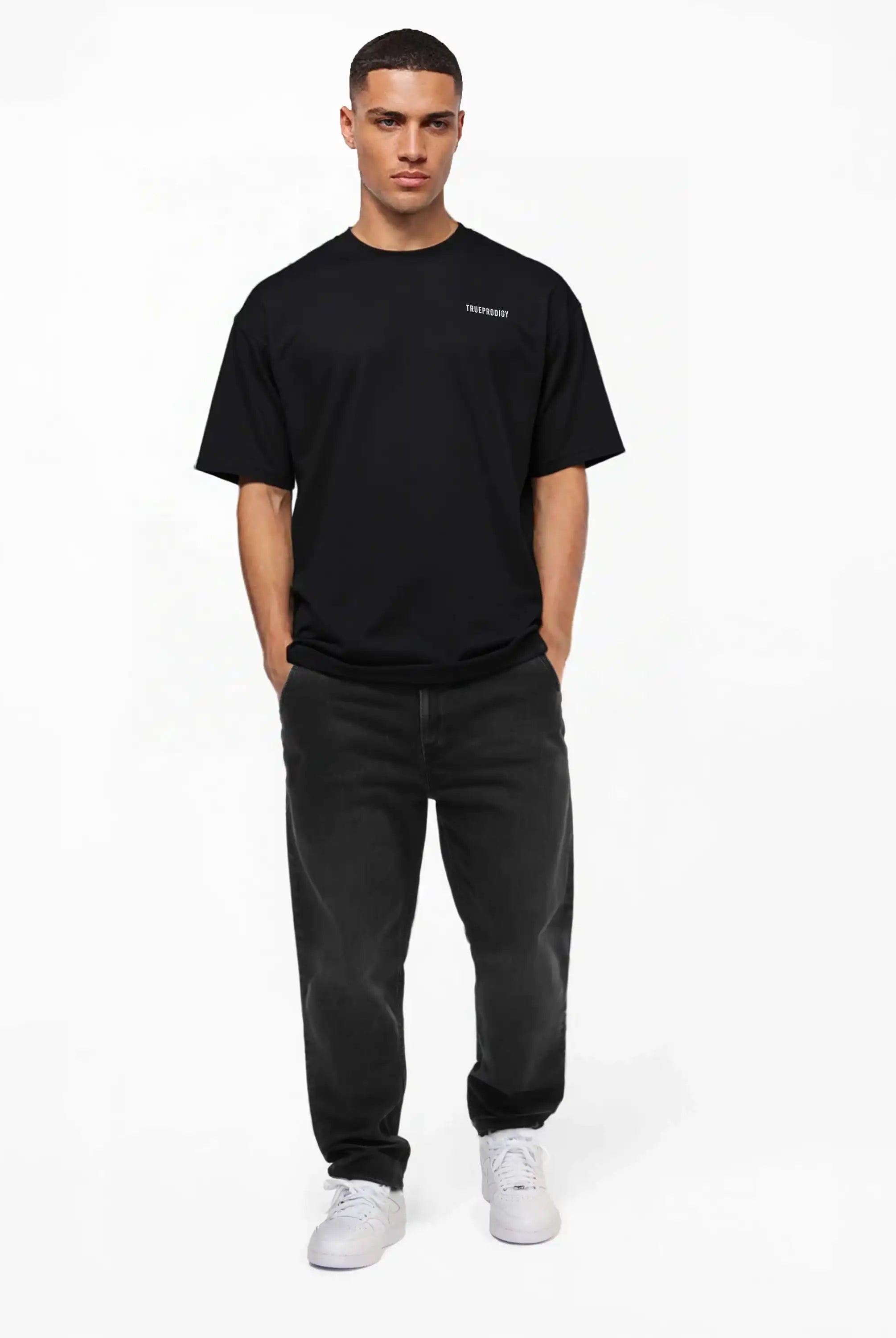 Eine Person steht mit dem Gesicht nach vorne vor einem schlichten weißen Hintergrund und trägt das trueprodigy Lior Oversize-T-Shirt mit Brustlogo und Rückenprint "never back down", dunkle Jeans und weiße Turnschuhe mit den Händen in den Taschen.