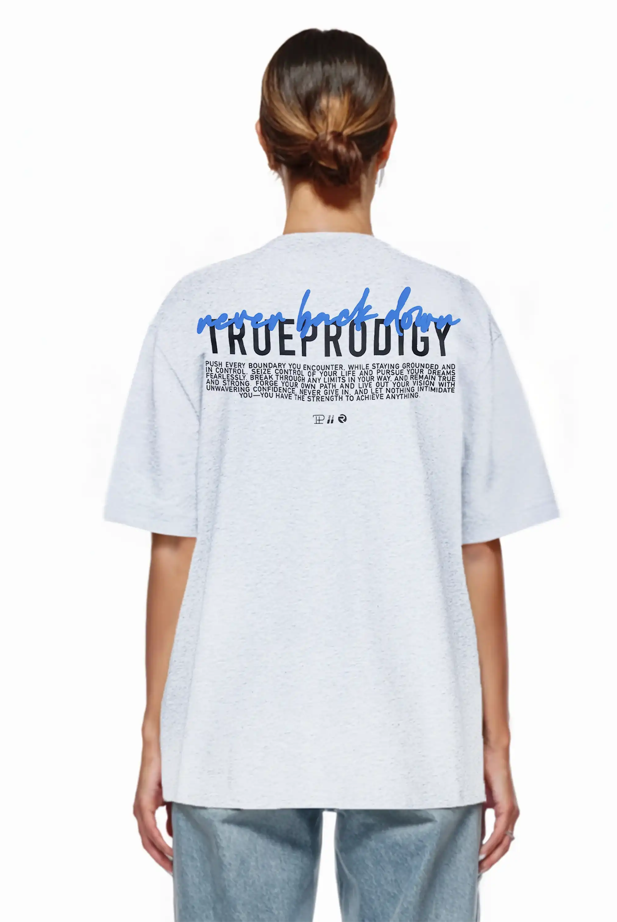 Person mit braunen Haaren in einem tiefen Dutt, trägt ein hellgraues trueprodigy Lior F Oversize-Damen-T-Shirt mit "never back down" Rückenstatement und blaue Jeans, von hinten gezeigt. Das T-Shirt ist aus schwerem Jerseystoff gefertigt.