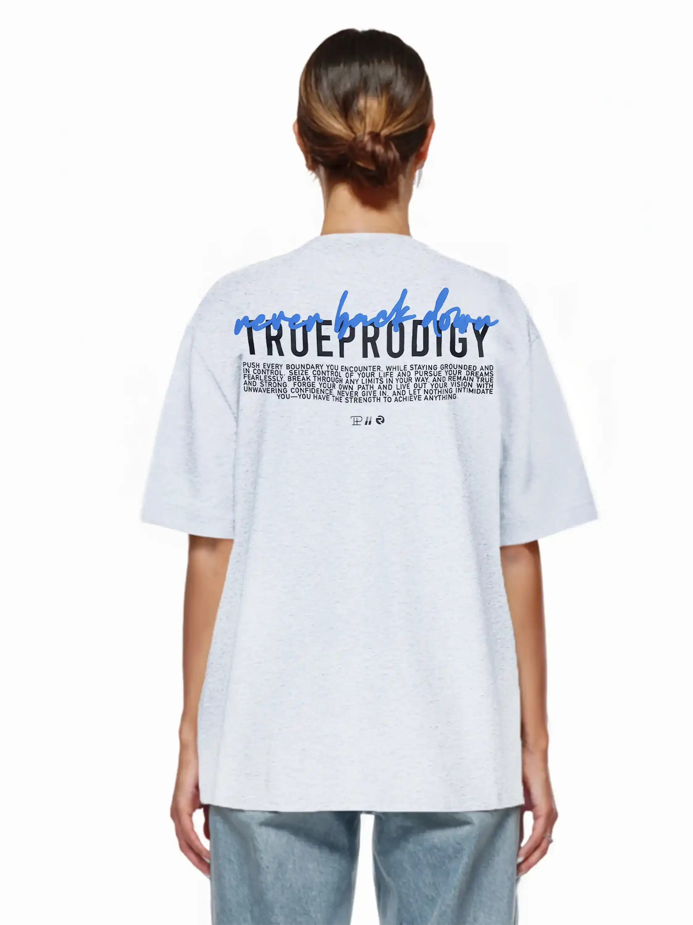 Person mit braunen Haaren in einem tiefen Dutt, trägt ein hellgraues trueprodigy Lior F Oversize-Damen-T-Shirt mit "never back down" Rückenstatement und blaue Jeans, von hinten gezeigt. Das T-Shirt ist aus schwerem Jerseystoff gefertigt.