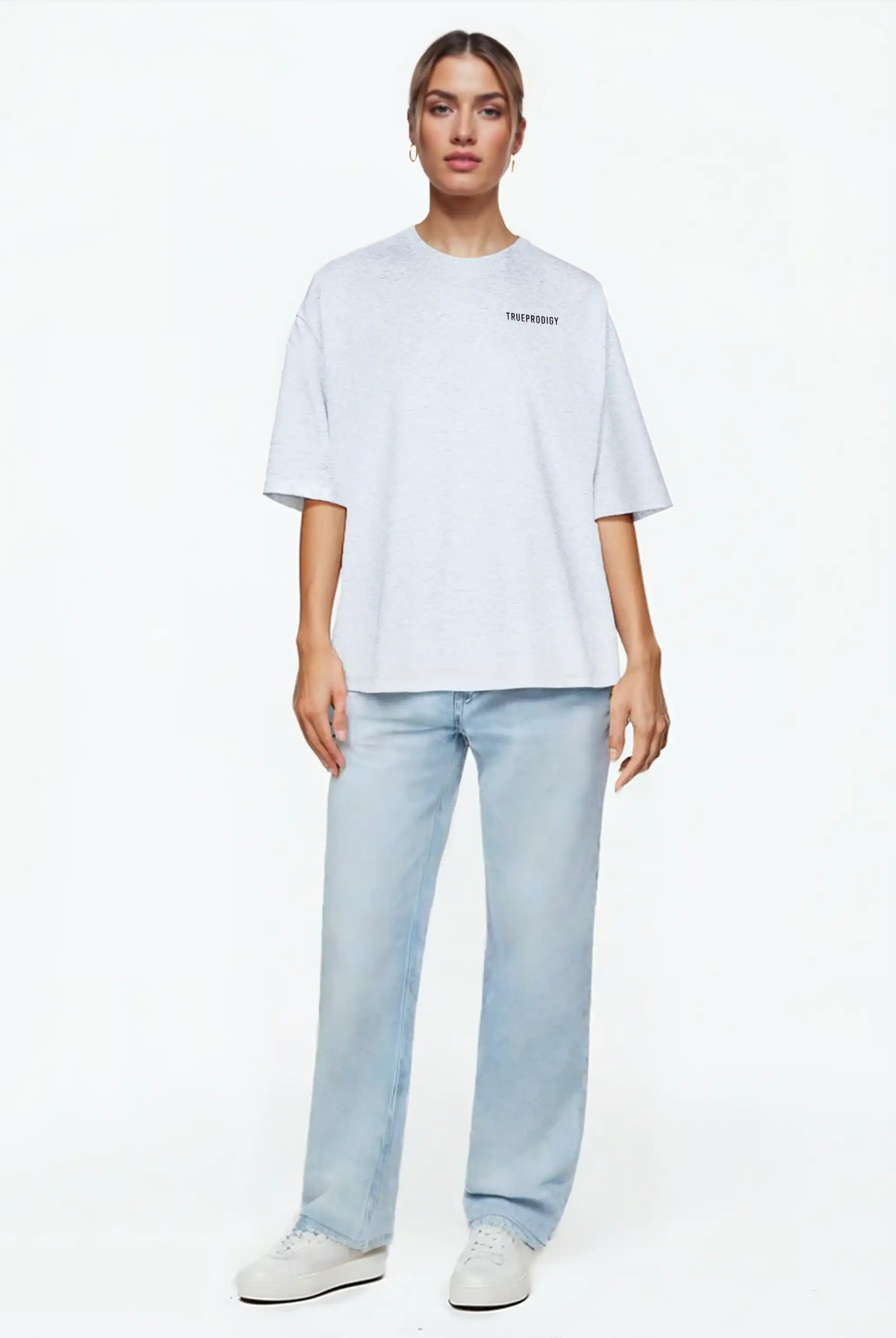 Eine Person steht mit dem Blick nach vorne, trägt das trueprodigy Lior F Oversize-Damen-T-Shirt mit Rückenstatement "never back down", hellblaue Jeans und weiße Turnschuhe vor einem schlichten weißen Hintergrund.