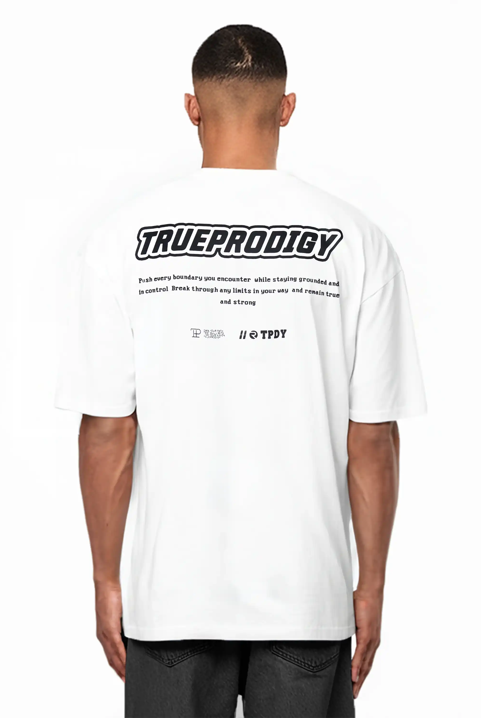 Eine Person mit kurzen Haaren trägt dunkle Shorts und das Eden Oversize-Shirt von trueprodigy aus schwerem Jersey, mit einem großen 3D-Logo-Schaumstoffdruck und kleinerem Text auf dem Rücken.