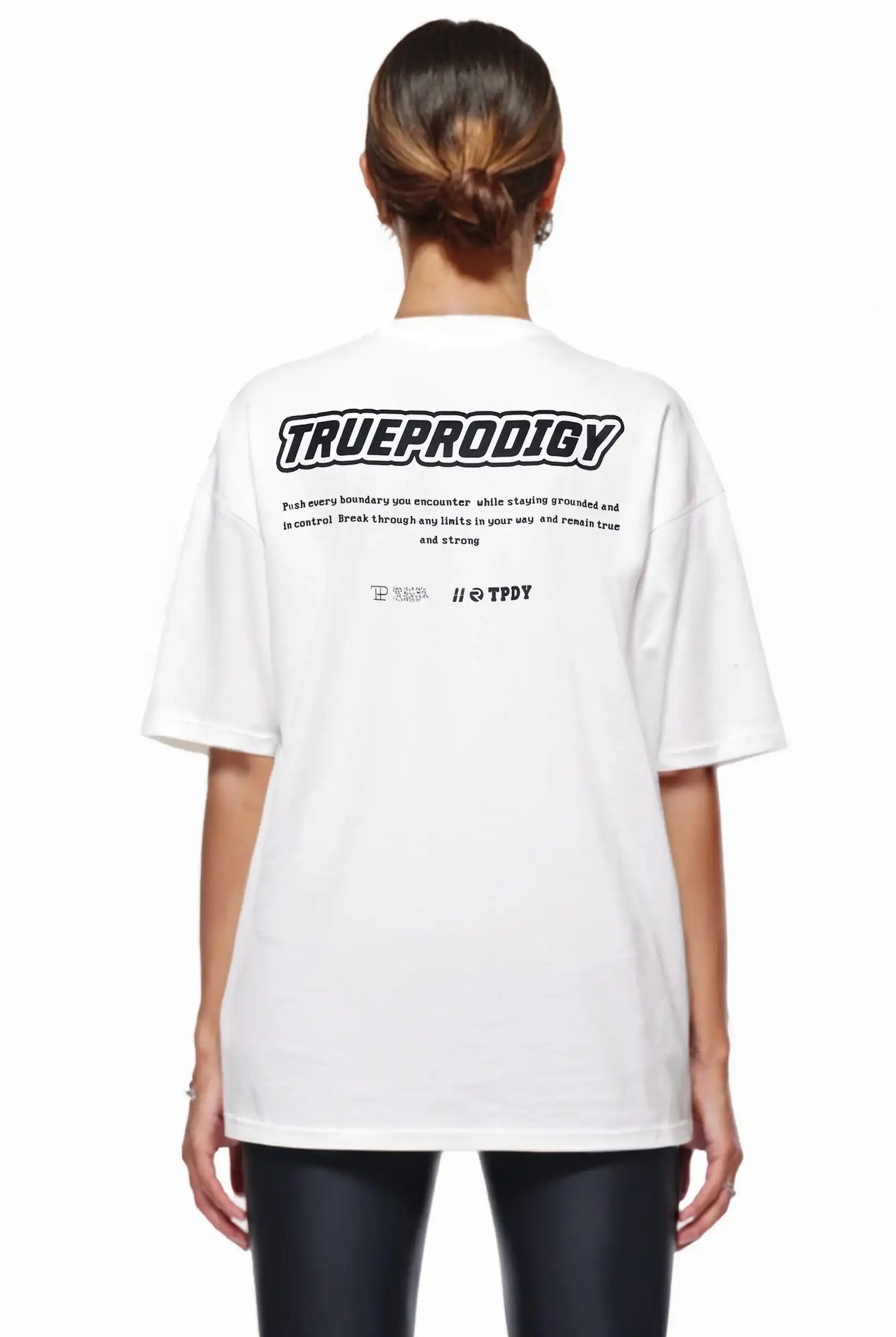 Eine Person mit braunen Haaren in einem tiefen Dutt trägt das trueprodigy Eden F Oversize-T-Shirt mit 3D-Logo-Schriftzug vorn & großem Rückenprint, von der Kamera abgewandt.