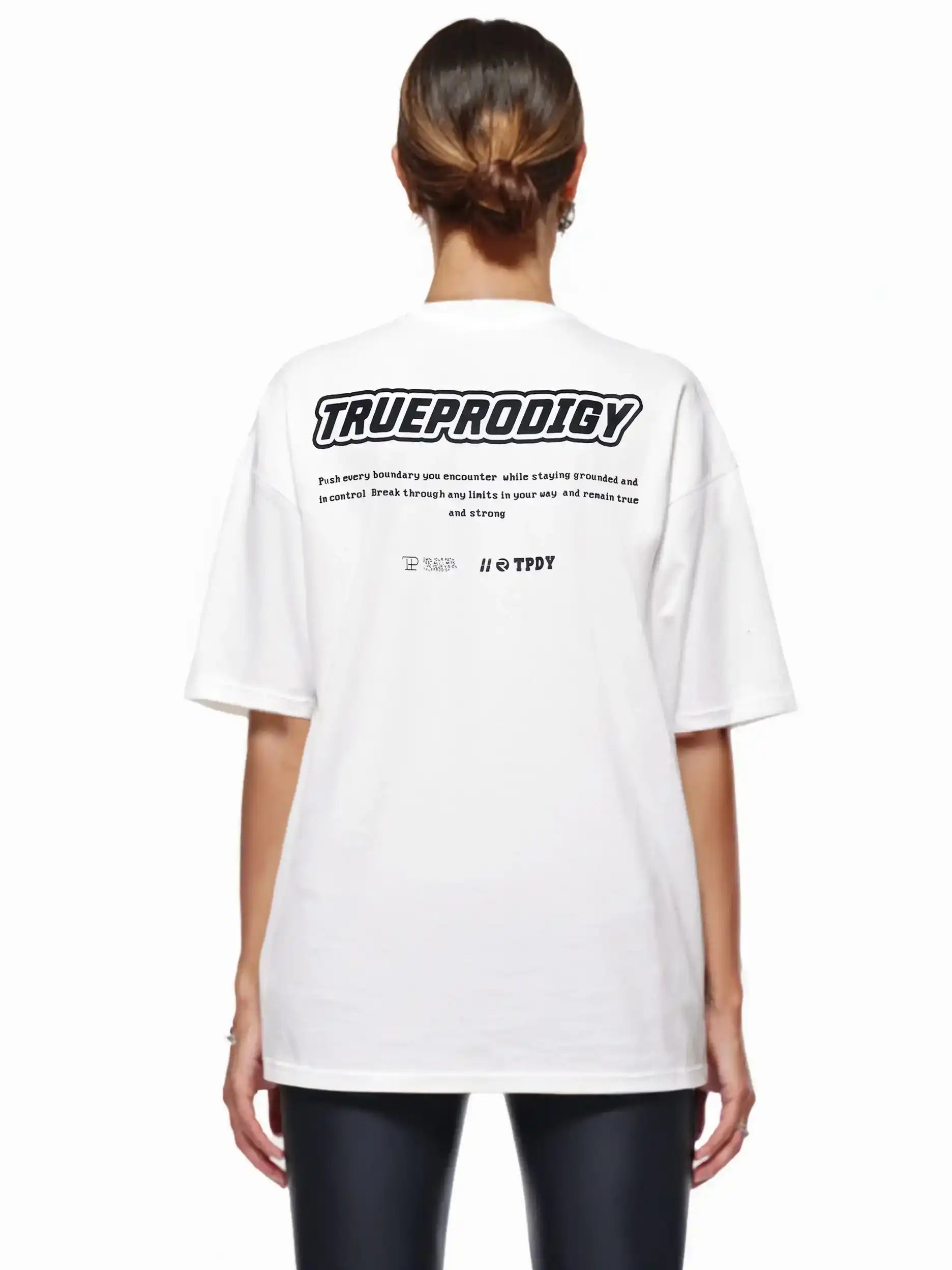 Eine Person mit braunen Haaren in einem tiefen Dutt trägt das trueprodigy Eden F Oversize-T-Shirt mit 3D-Logo-Schriftzug vorn & großem Rückenprint, von der Kamera abgewandt.