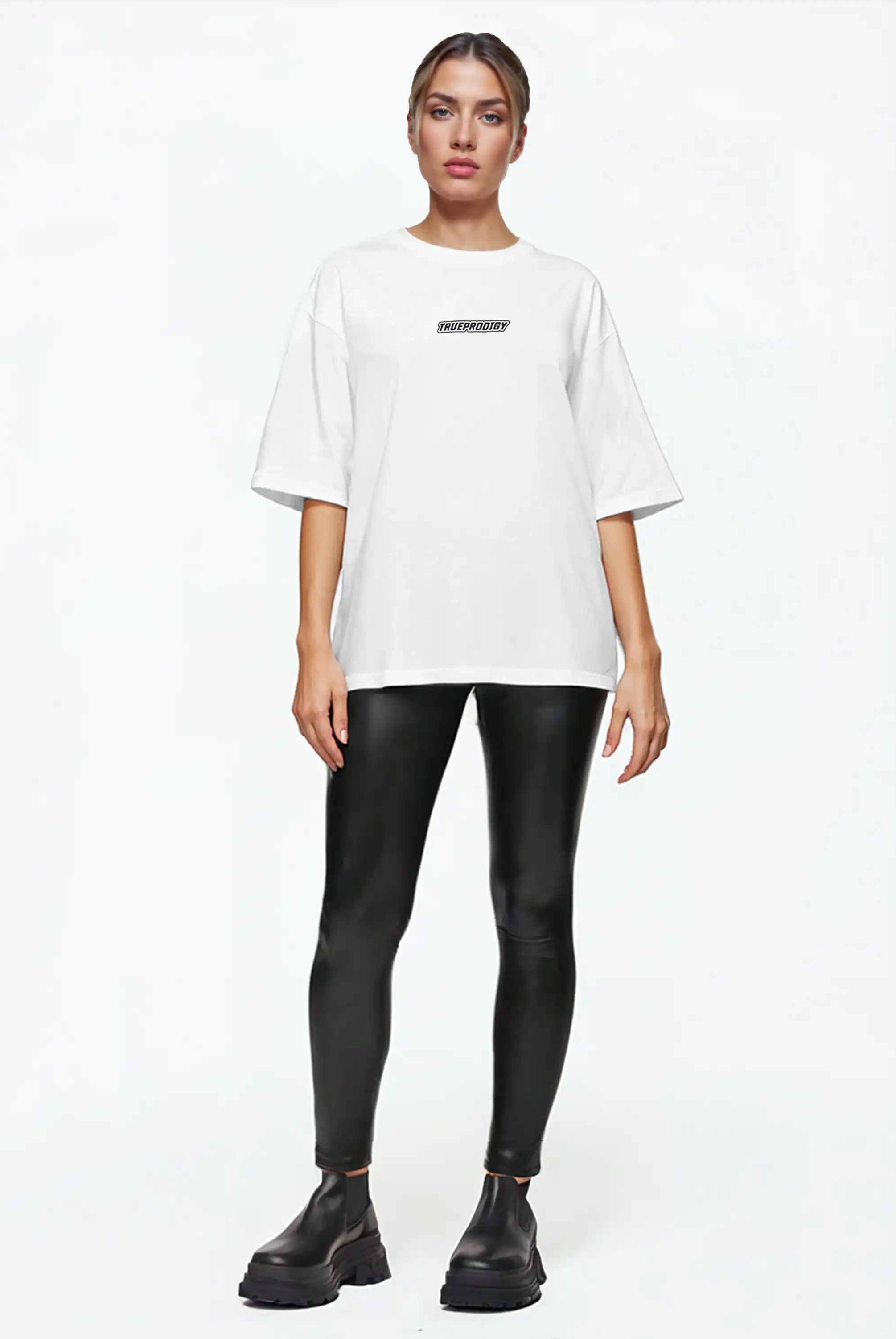 Eine Person steht mit dem Gesicht nach vorne vor einem schlichten weißen Hintergrund und trägt ein trueprodigy Eden F Oversize-T-Shirt mit 3D-Logo-Schriftzug vorn & großem Rückenprint, schwarze Leggings in Lederoptik und schwarze, klobige Schuhe.
