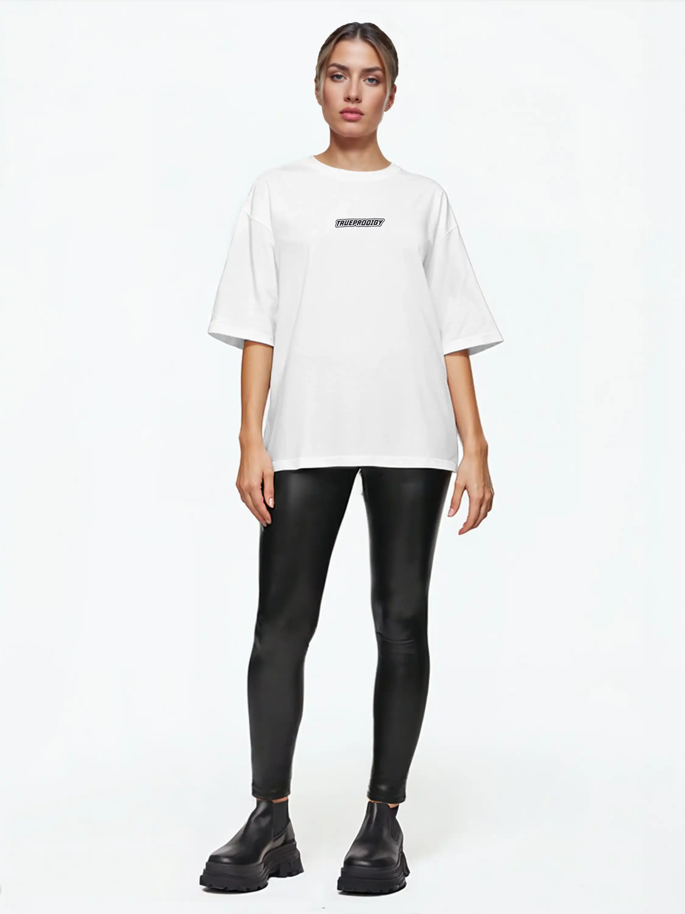 Eine Person steht mit dem Gesicht nach vorne vor einem schlichten weißen Hintergrund und trägt ein trueprodigy Eden F Oversize-T-Shirt mit 3D-Logo-Schriftzug vorn & großem Rückenprint, schwarze Leggings in Lederoptik und schwarze, klobige Schuhe.