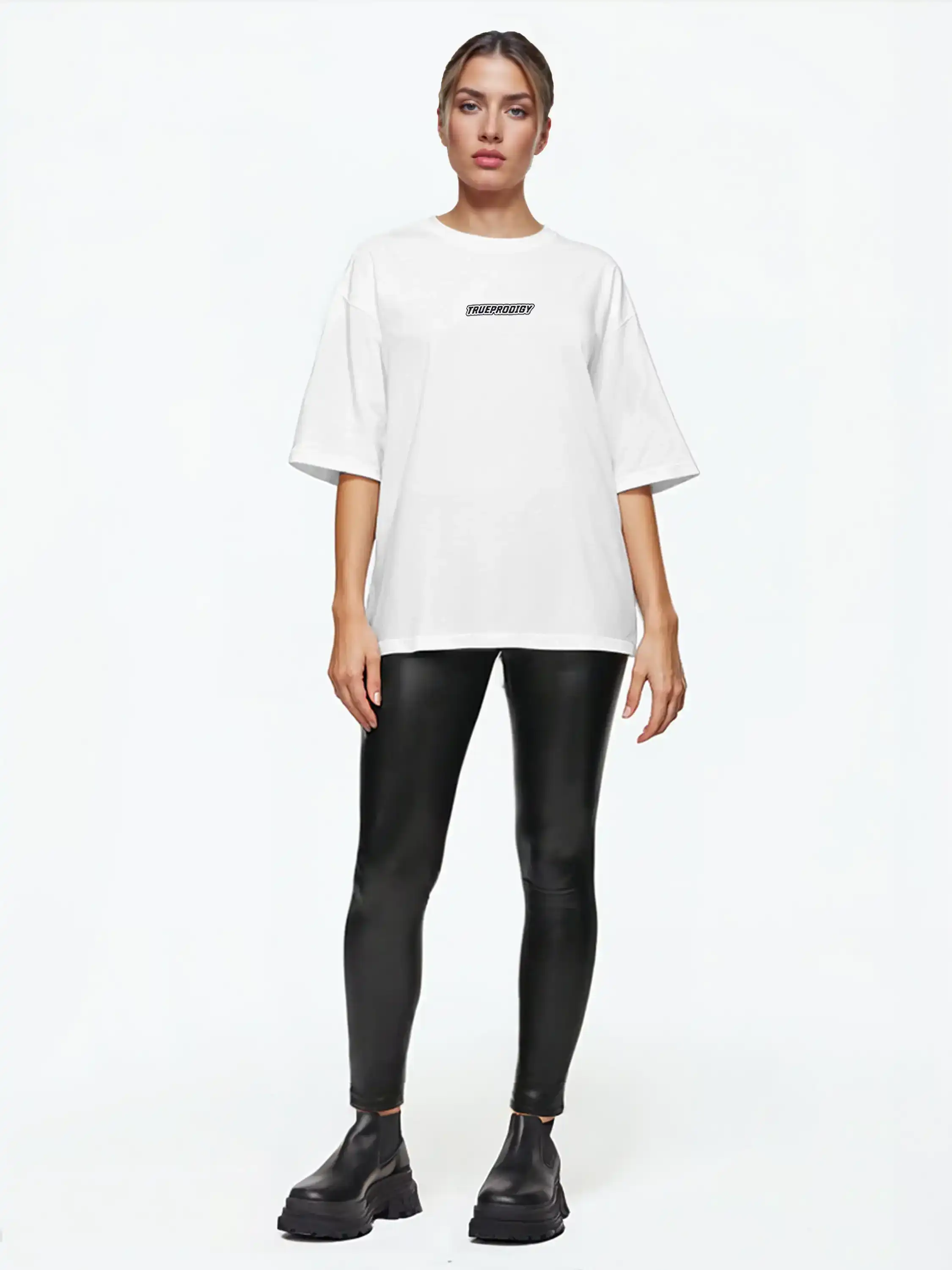 Eine Person steht mit dem Gesicht nach vorne vor einem schlichten weißen Hintergrund und trägt ein trueprodigy Eden F Oversize-T-Shirt mit 3D-Logo-Schriftzug vorn & großem Rückenprint, schwarze Leggings in Lederoptik und schwarze, klobige Schuhe.