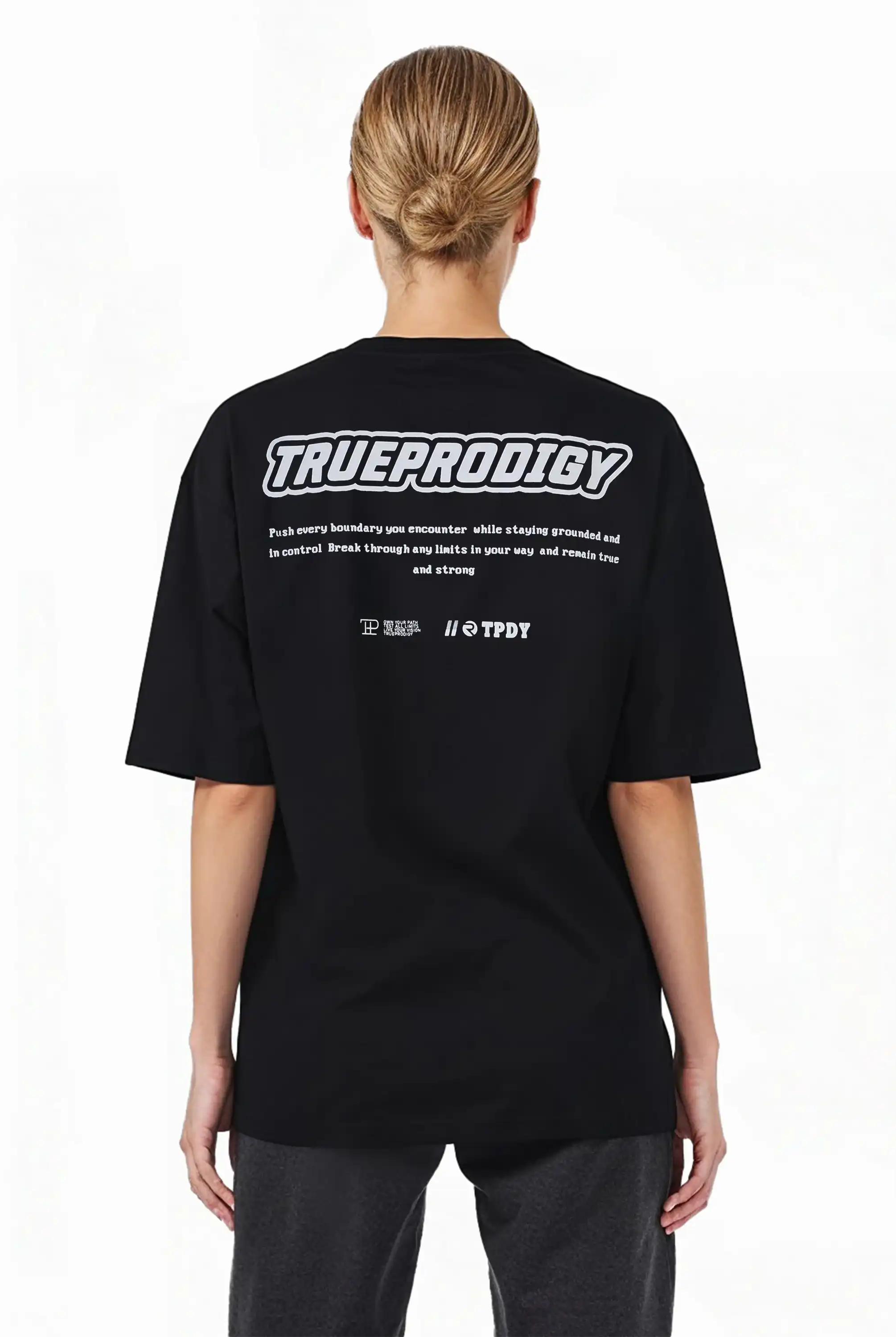 Eine Person mit hellen Haaren in einem tiefen Dutt modelliert das Eden F Oversize-T-Shirt von trueprodigy, mit schwerem Jerseystoff und einem auffälligen 3D-Logo-Schriftzug auf der Vorderseite sowie einem großen Rückenprint auf der Rückseite.