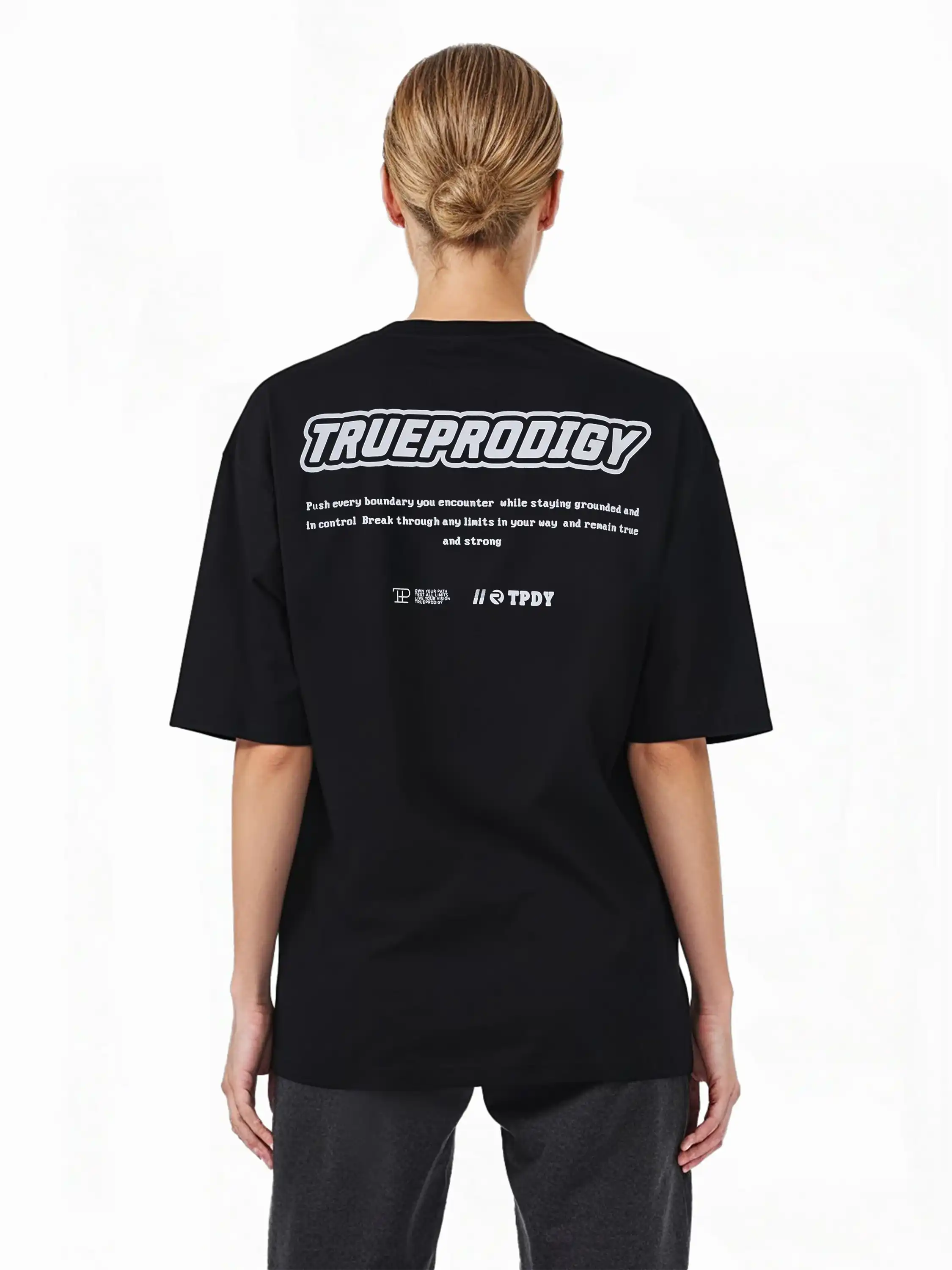 Eine Person mit hellen Haaren in einem tiefen Dutt modelliert das Eden F Oversize-T-Shirt von trueprodigy, mit schwerem Jerseystoff und einem auffälligen 3D-Logo-Schriftzug auf der Vorderseite sowie einem großen Rückenprint auf der Rückseite.