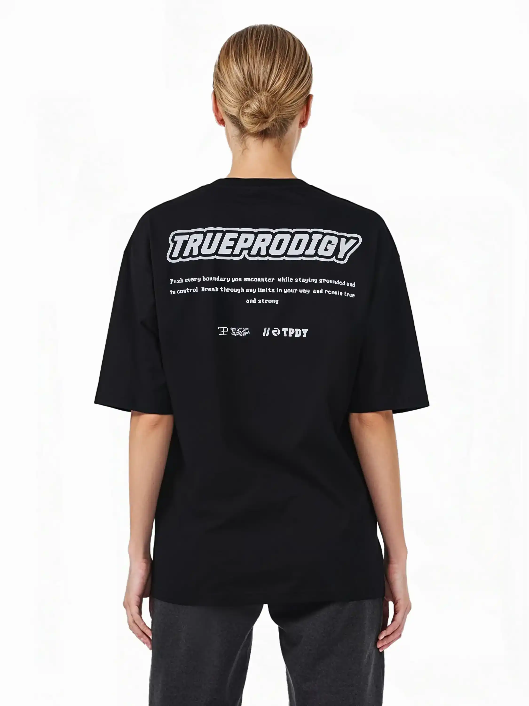 Eine Person mit hellen Haaren in einem tiefen Dutt modelliert das Eden F Oversize-T-Shirt von trueprodigy, mit schwerem Jerseystoff und einem auffälligen 3D-Logo-Schriftzug auf der Vorderseite sowie einem großen Rückenprint auf der Rückseite.