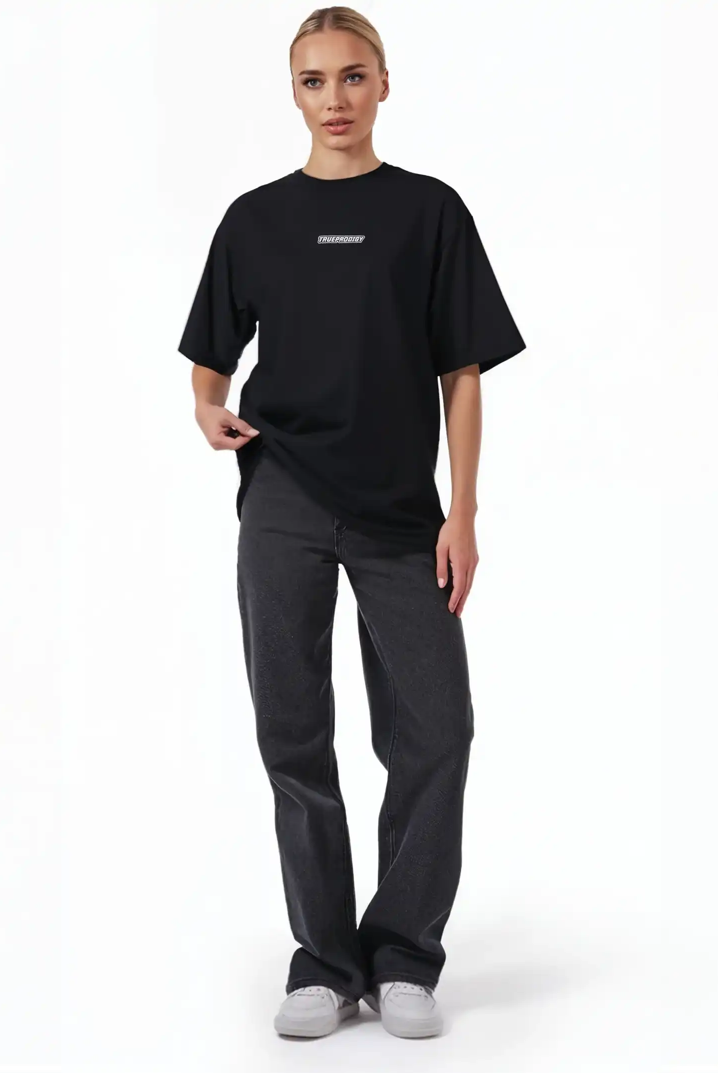 Eine Person steht mit dem Blick nach vorne und trägt das schwarze trueprodigy Eden F Oversize-T-Shirt mit 3D-Logo-Schriftzug vorn & großem Rückenprint, gepaart mit dunklen Straight-Leg-Jeans und weißen Sneakers vor einem schlichten weißen Hintergrund.