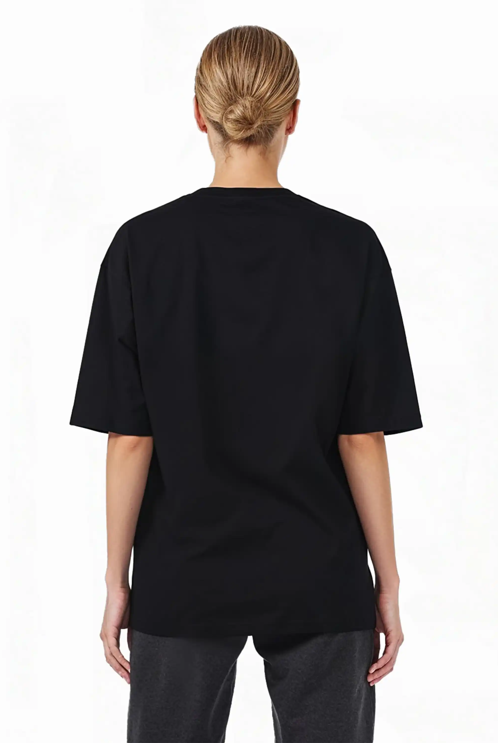 Eine Person mit hellen Haaren in einem tiefen Dutt ist von hinten zu sehen. Sie trägt das trueprodigy Haram F Oversize-T-Shirt mit TPDY-Stickerei & cleaner Optik und eine dunkle Hose vor einem schlichten weißen Hintergrund.