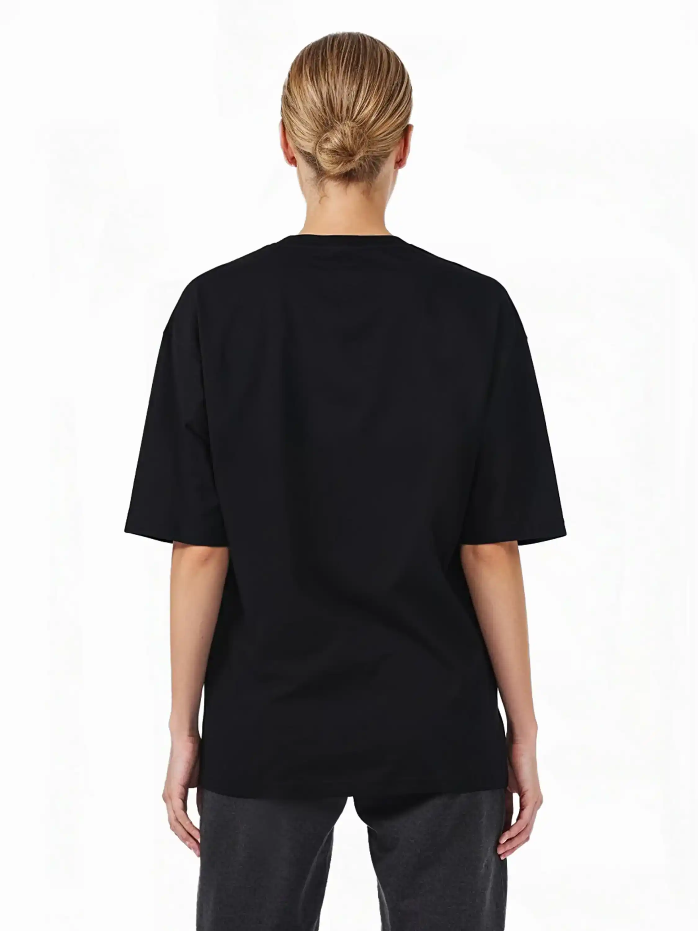 Eine Person mit hellen Haaren in einem tiefen Dutt ist von hinten zu sehen. Sie trägt das trueprodigy Haram F Oversize-T-Shirt mit TPDY-Stickerei & cleaner Optik und eine dunkle Hose vor einem schlichten weißen Hintergrund.