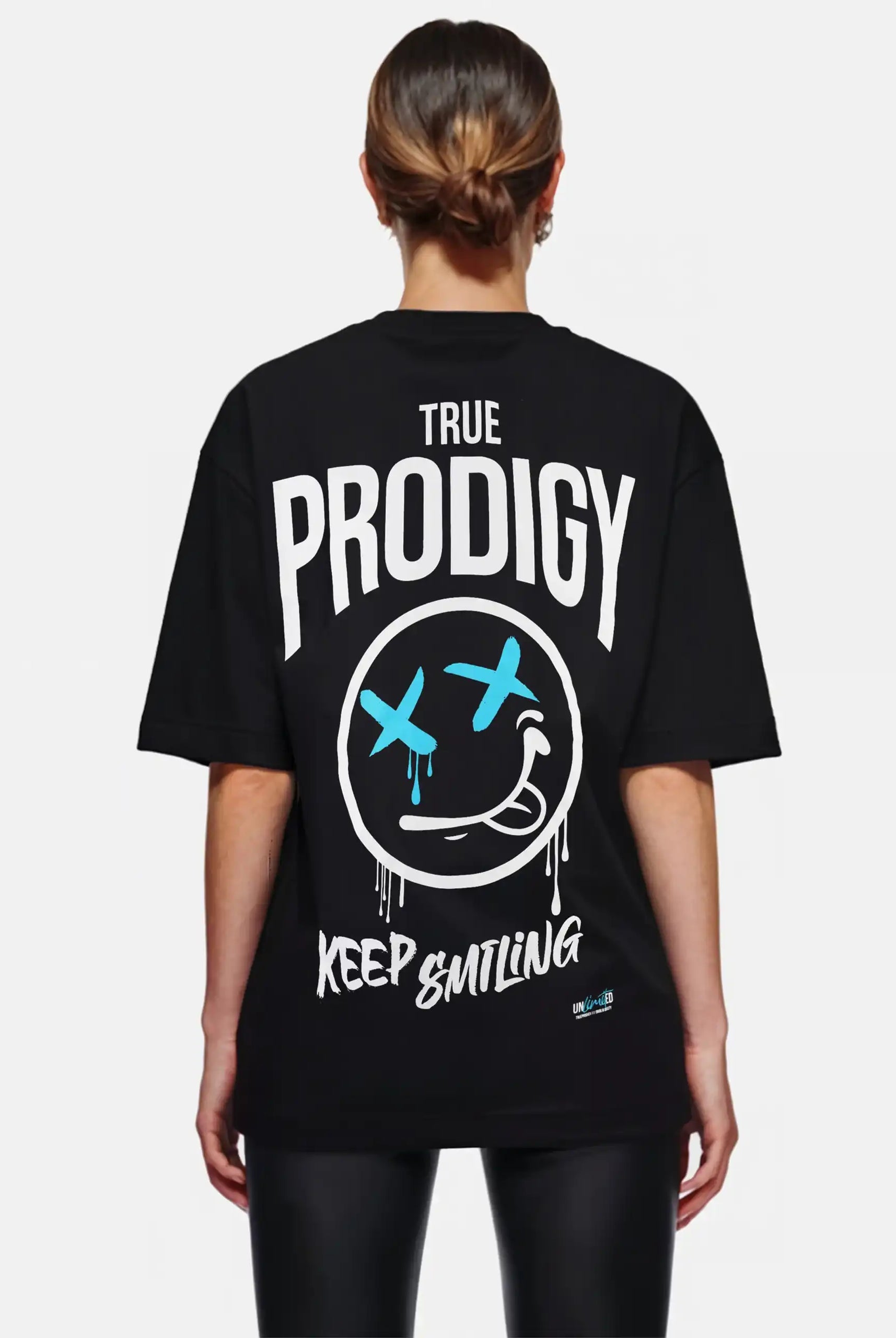 Eine Person mit hellbraunem, nach hinten gebundenem Haar trägt ein schwarzes Trueprodigy Kenji F Oversize-Damen-T-Shirt mit Graffiti-Aufdrucken und einer großen Distressed Face-Grafik mit blauen X-Augen und einem Stirnrunzeln auf dem Rücken.