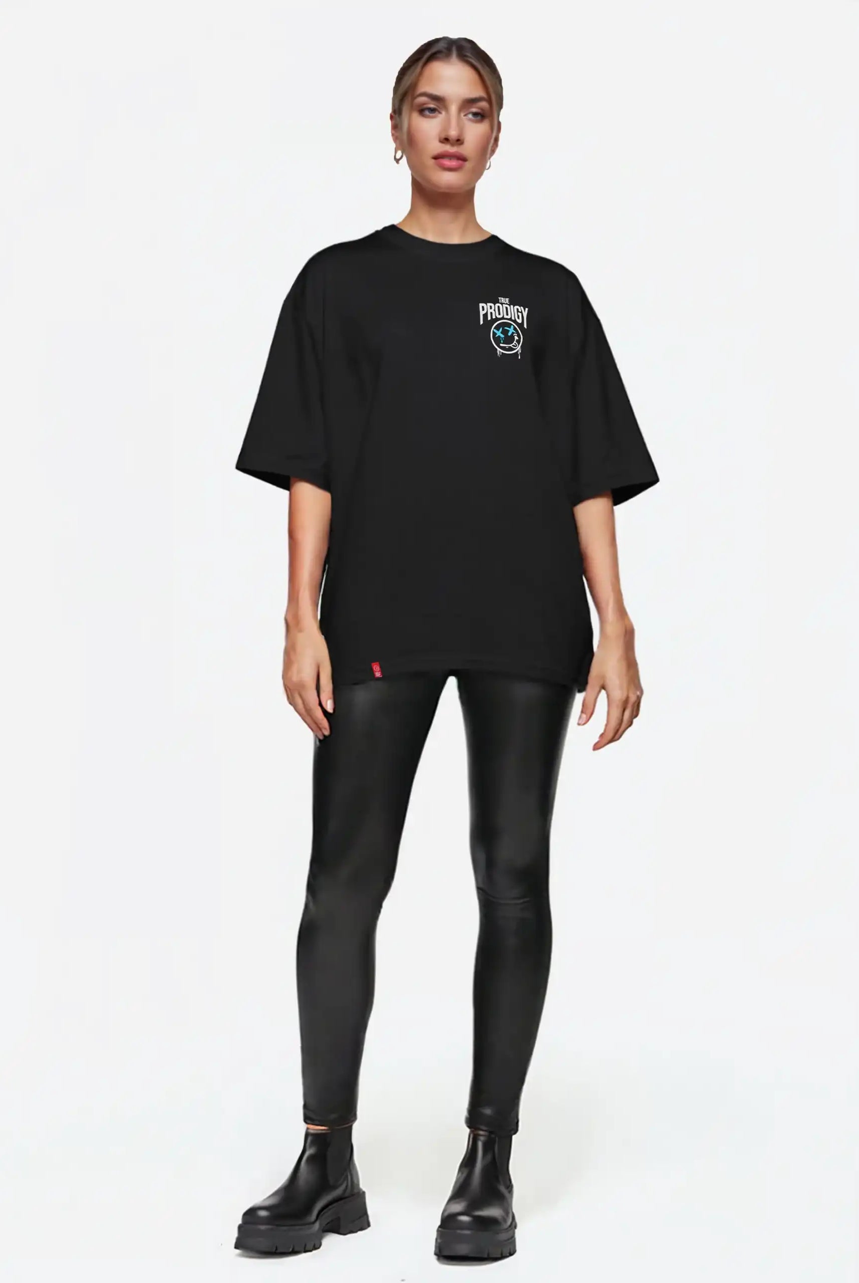 Eine Person steht mit dem Blick nach vorne und trägt das trueprodigy Kenji F Oversize-Damen-T-Shirt mit Graffiti-Brust- und Rückenprint, schwarze Kunstleder-Leggings und schwarze Ankle Boots vor einem schlichten weißen Hintergrund.