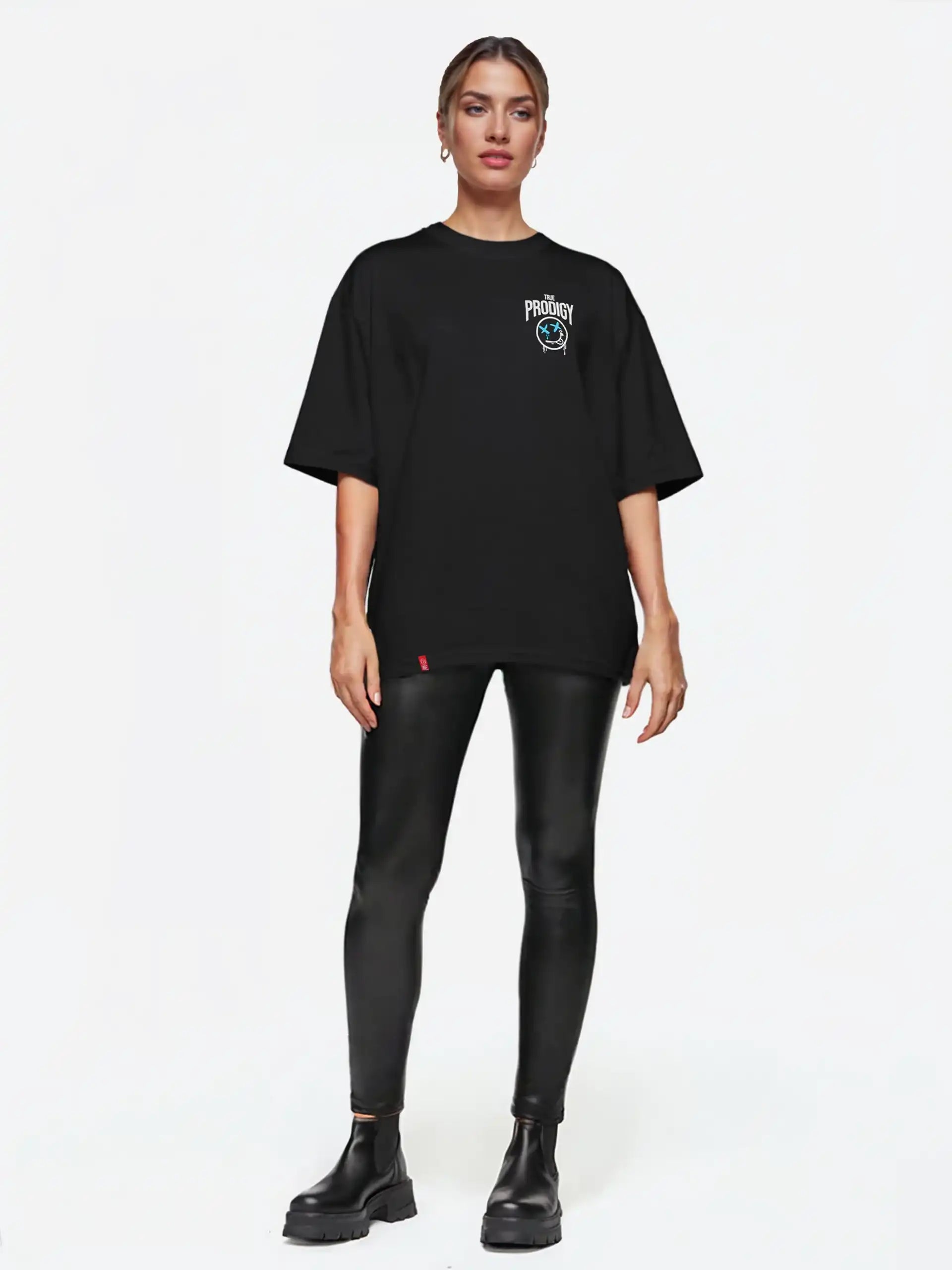 Eine Person steht mit dem Blick nach vorne und trägt das trueprodigy Kenji F Oversize-Damen-T-Shirt mit Graffiti-Brust- und Rückenprint, schwarze Kunstleder-Leggings und schwarze Ankle Boots vor einem schlichten weißen Hintergrund.