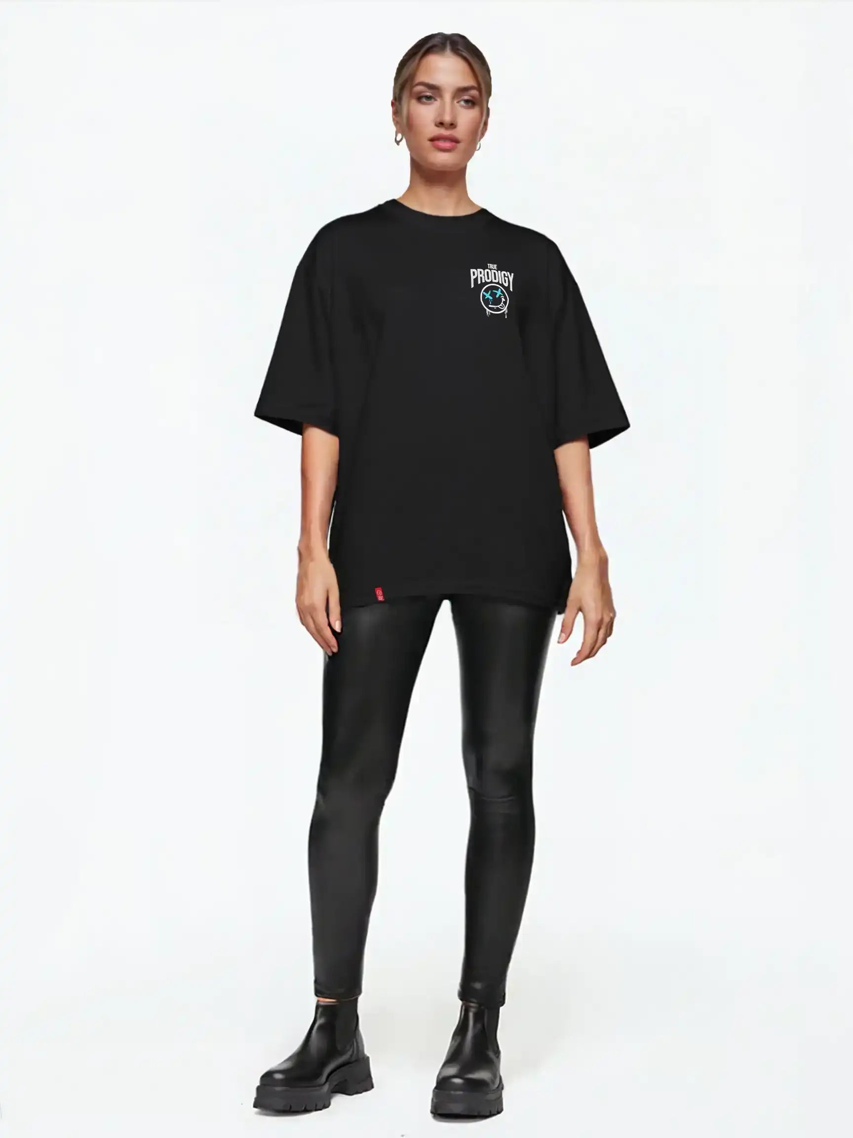 Eine Person steht vor einem schlichten weißen Hintergrund und trägt das trueprodigy Kenji F Oversize-Damen-T-Shirt mit Graffiti-Brust- und Rückenprint, gepaart mit glänzenden schwarzen Leggings und schwarzen Ankle Boots.
