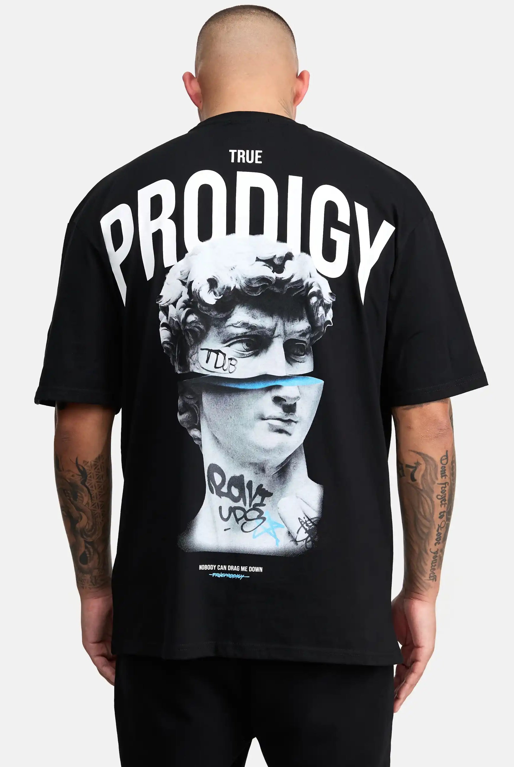 Eine Person mit rasiertem Kopf ist von hinten zu sehen und trägt das Bengi Oversized T-Shirt mit Druck von trueprodigy, das aus schwerem Jersey-Stoff besteht und eine Michelangelo's David-Grafik mit Graffiti-Details und fetten Schriftzügen aufweist.