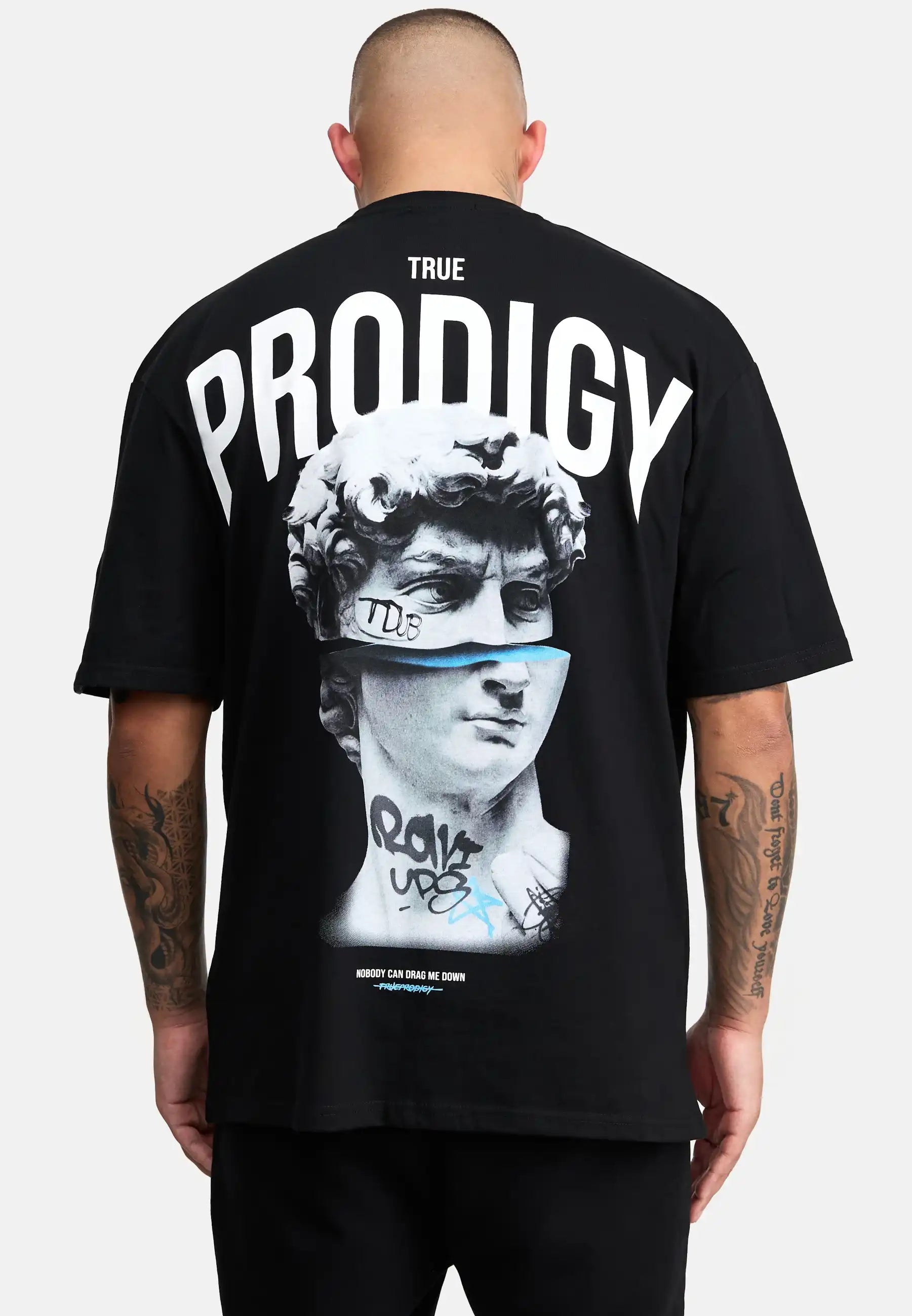 Eine Person mit rasiertem Kopf ist von hinten zu sehen und trägt das Bengi Oversized T-Shirt mit Druck von trueprodigy, das aus schwerem Jersey-Stoff besteht und eine Michelangelo's David-Grafik mit Graffiti-Details und fetten Schriftzügen aufweist.