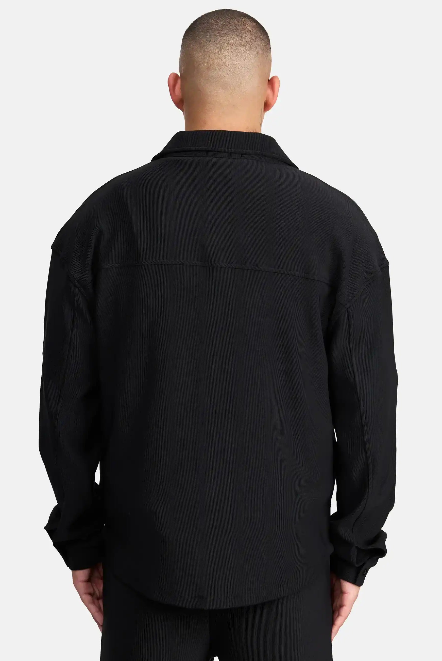 Eine Person mit kurz geschnittenem Haar wird von hinten gezeigt, die ein Trueprodigy Wyatt Oversized Langarm Hemd und eine schwarze Hose vor einem schlichten weißen Hintergrund trägt.