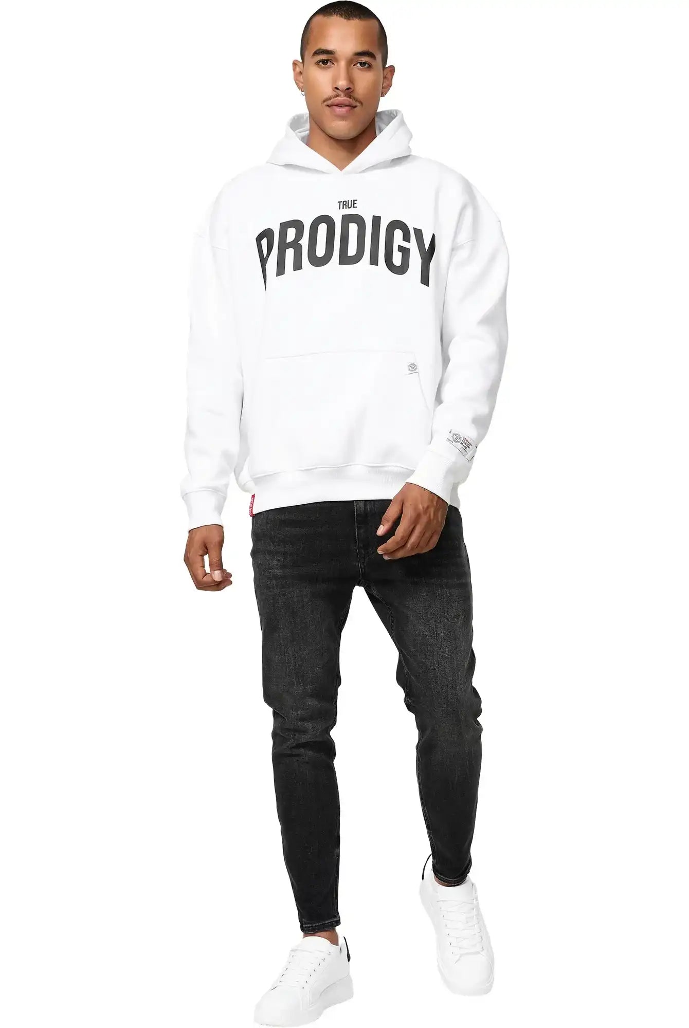 Ein Mann blickt nach vorne in einem trueprodigy Tobi Oversized Hoodie mit Print, mit fetten schwarzen Schriftzügen, gepaart mit schwarzen Jeans und weißen Turnschuhen, vor einem schlichten weißen Hintergrund.
