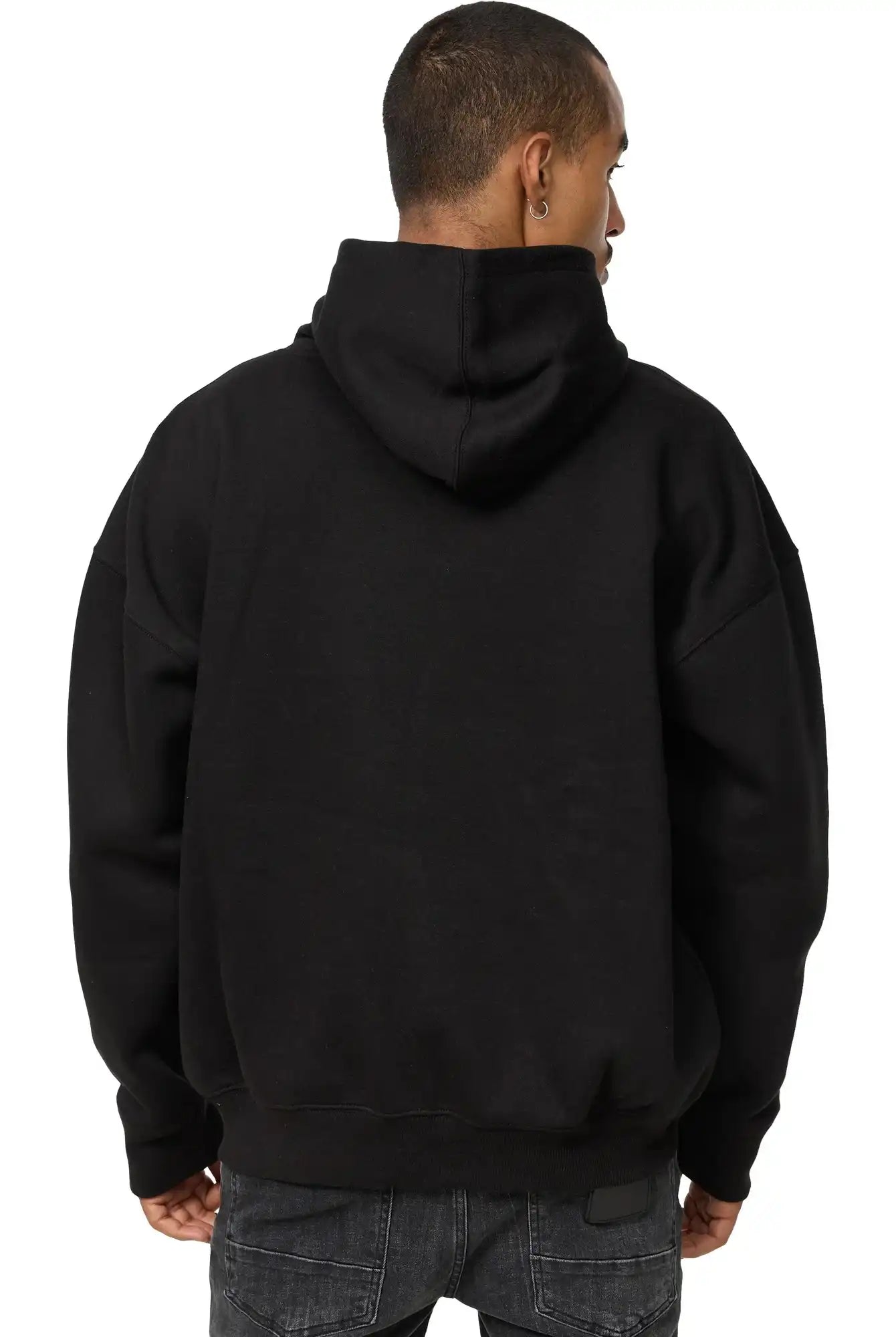 Gezeigt wird eine Person von hinten, die entspannt in einem schwarzen trueprodigy Tobi Oversized Hoodie mit Print und dunkler Jeans steht. Die Kapuze des Unisex Kapuzensweatshirts ist hochgezogen, bedeckt aber nicht ihren Kopf.