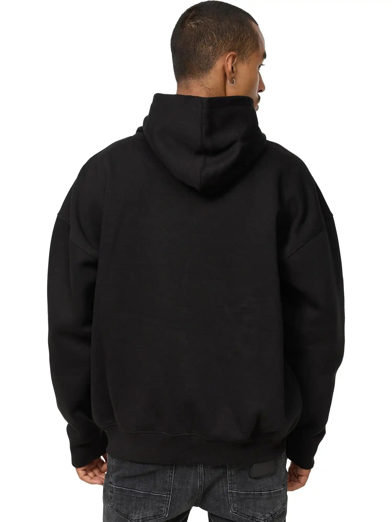 Gezeigt wird eine Person von hinten, die entspannt in einem schwarzen trueprodigy Tobi Oversized Hoodie mit Print und dunkler Jeans steht. Die Kapuze des Unisex Kapuzensweatshirts ist hochgezogen, bedeckt aber nicht ihren Kopf.