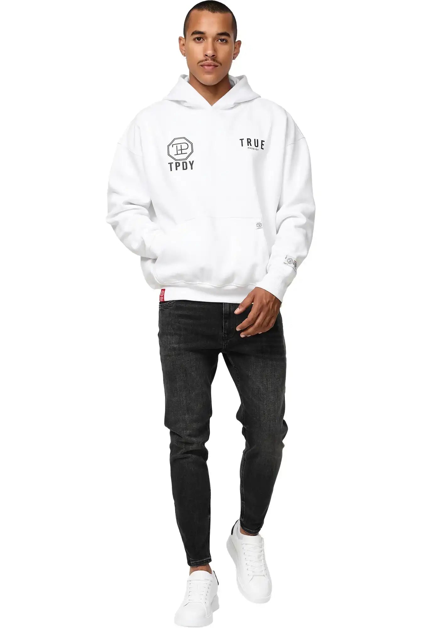 Ein Mann sieht nach vorne und trägt einen weißen trueprodigy Aaren Oversized Hoodie mit Print, schwarze Skinny Jeans und weiße Turnschuhe vor einem schlichten weißen Hintergrund.
