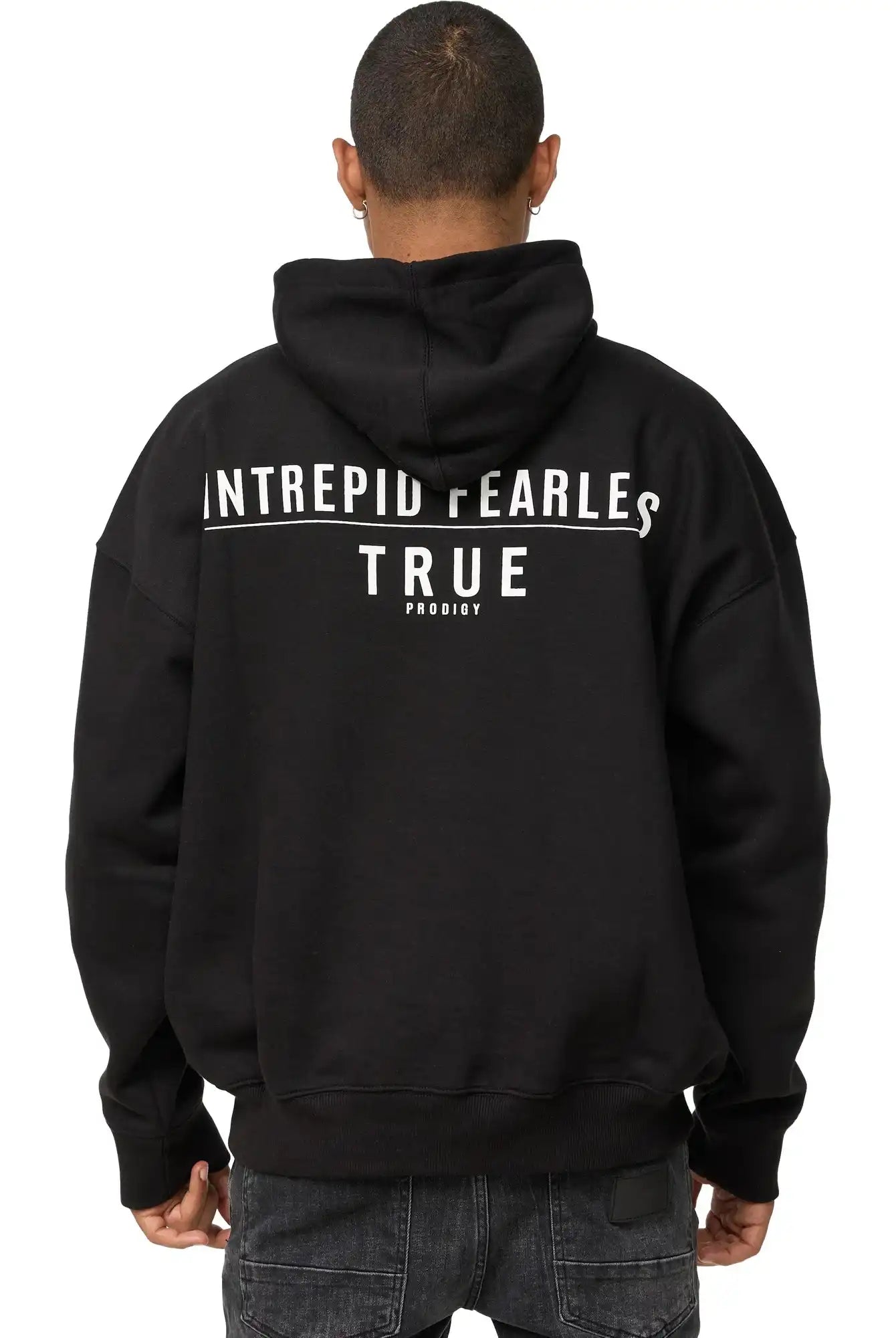 Eine Person, die den trueprodigy Aaren Oversized Hoodie mit Print in schwarz mit der Aufschrift "INTREPID FEARLESS TRUE PRODIGY" in weiß auf dem Rücken trägt, steht mit dem Rücken zur Kamera. Dieser Kapuzenpulli setzt ein mutiges Statement.