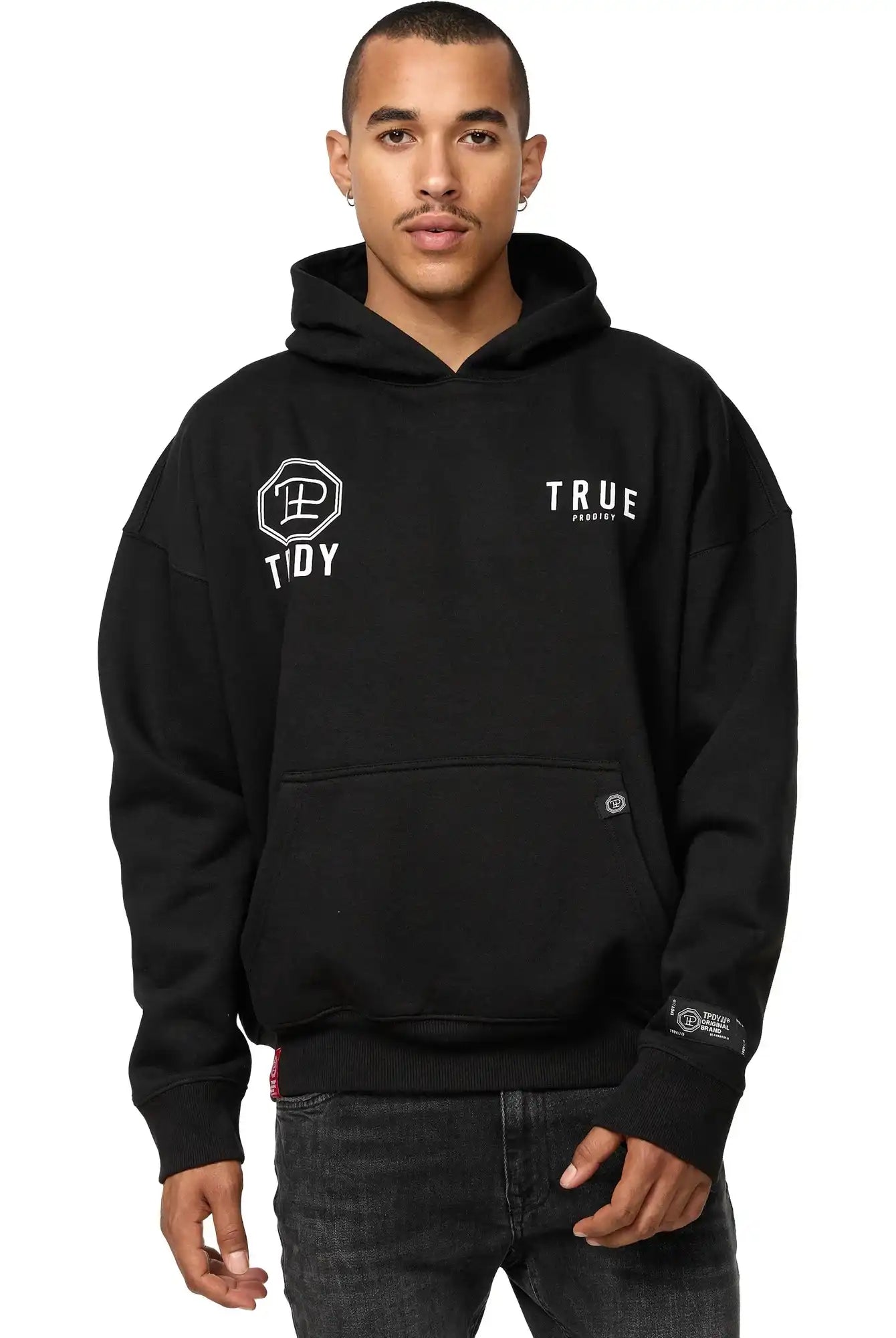 Eine Person steht mit Blick nach vorne in einem schwarzen, übergroßen trueprodigy Aaren Hoodie mit Print mit Fronttasche und weißem Logo, gepaart mit einer schwarzen Jeans vor einem schlichten weißen Hintergrund.